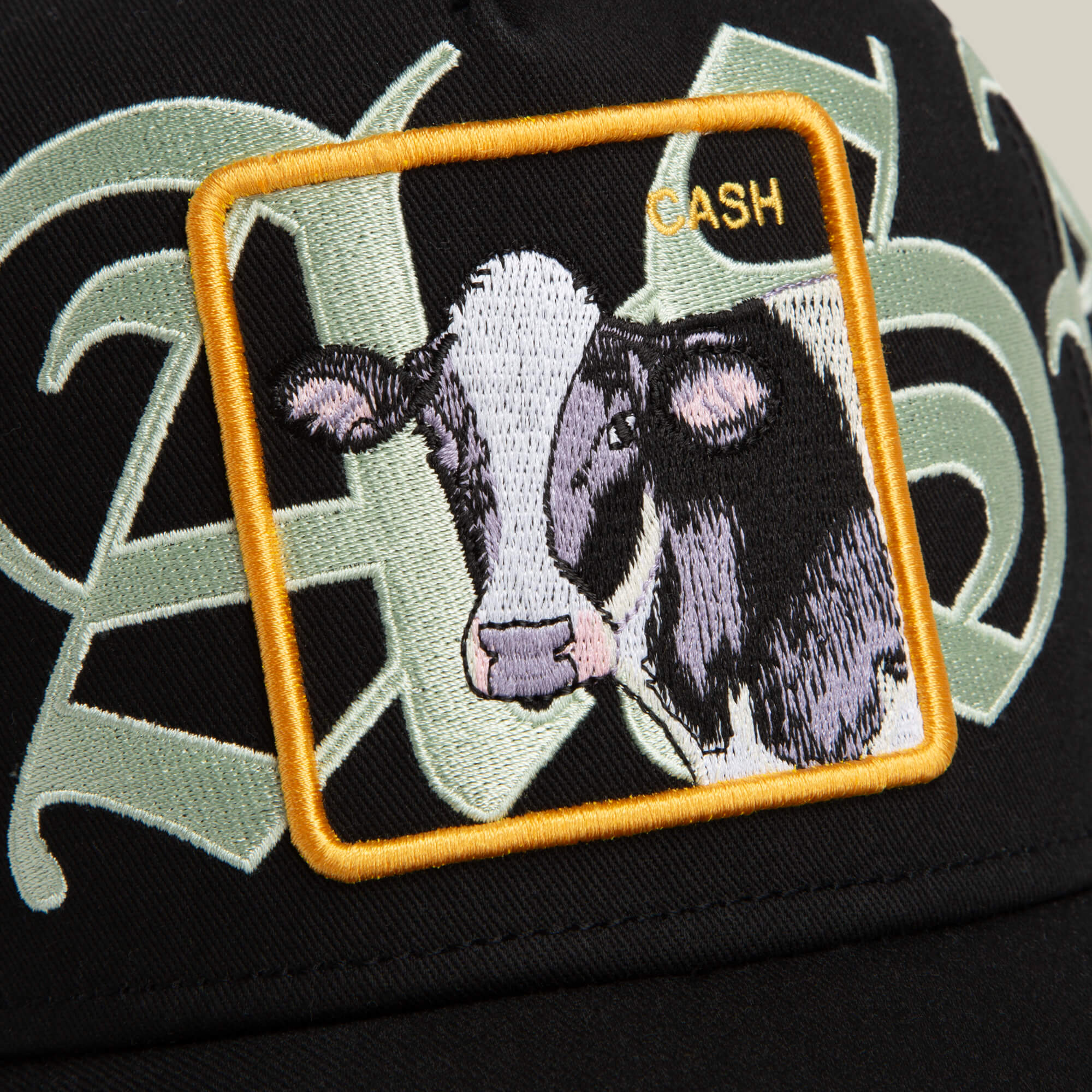 The Goorin Bros. Old English Cash hat is black with an ornate cow patch, a yellow square border, and bold yellow “CASH” lettering in Old English script.