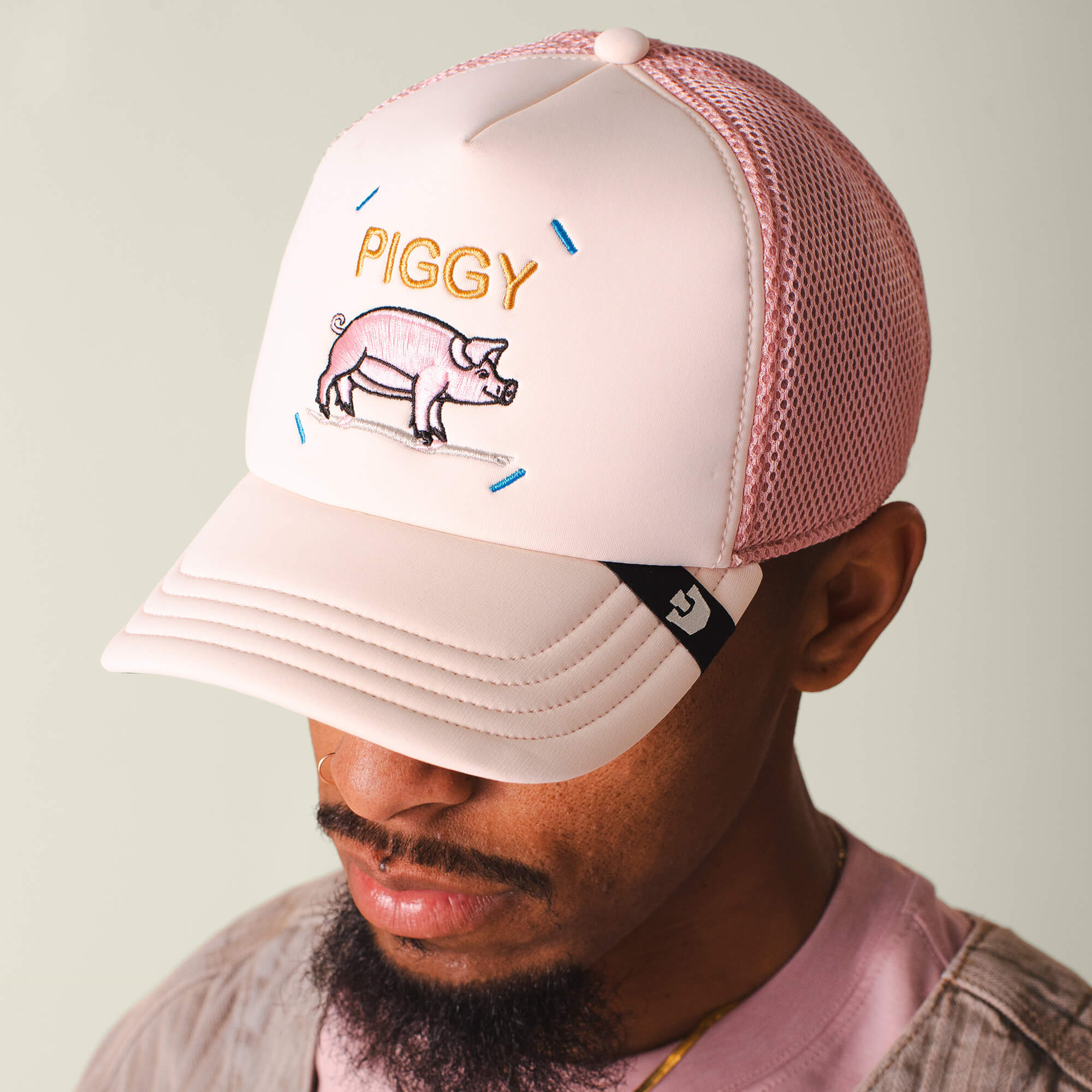 A man wears the Goorin Bros. Neo Farm - Piggy Pig hat, featuring a pig illustration and "PIGGY" stitched on the front, with a pink and white breathable mesh design.