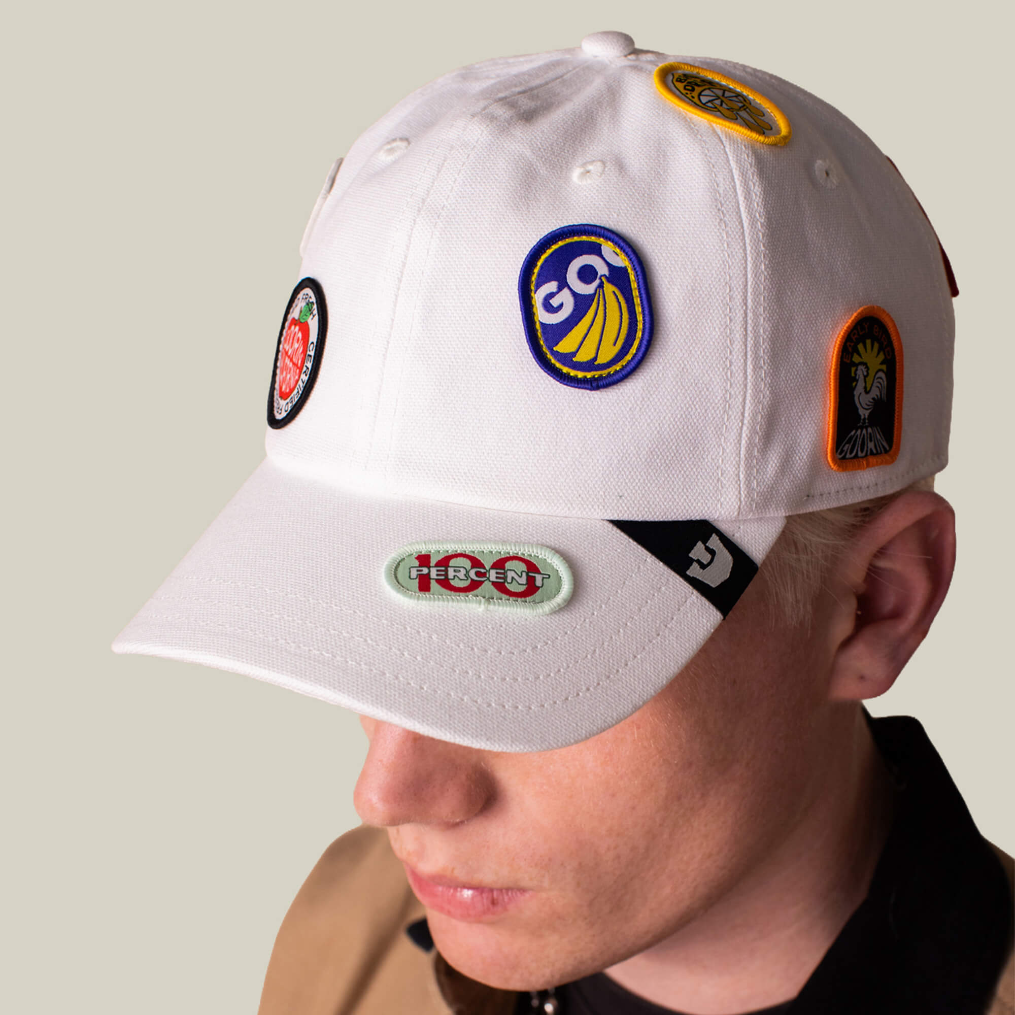 A person wears the Goorin Bros. Pop Appeal cap, a white canvas baseball hat adorned with assorted colorful embroidered badges.