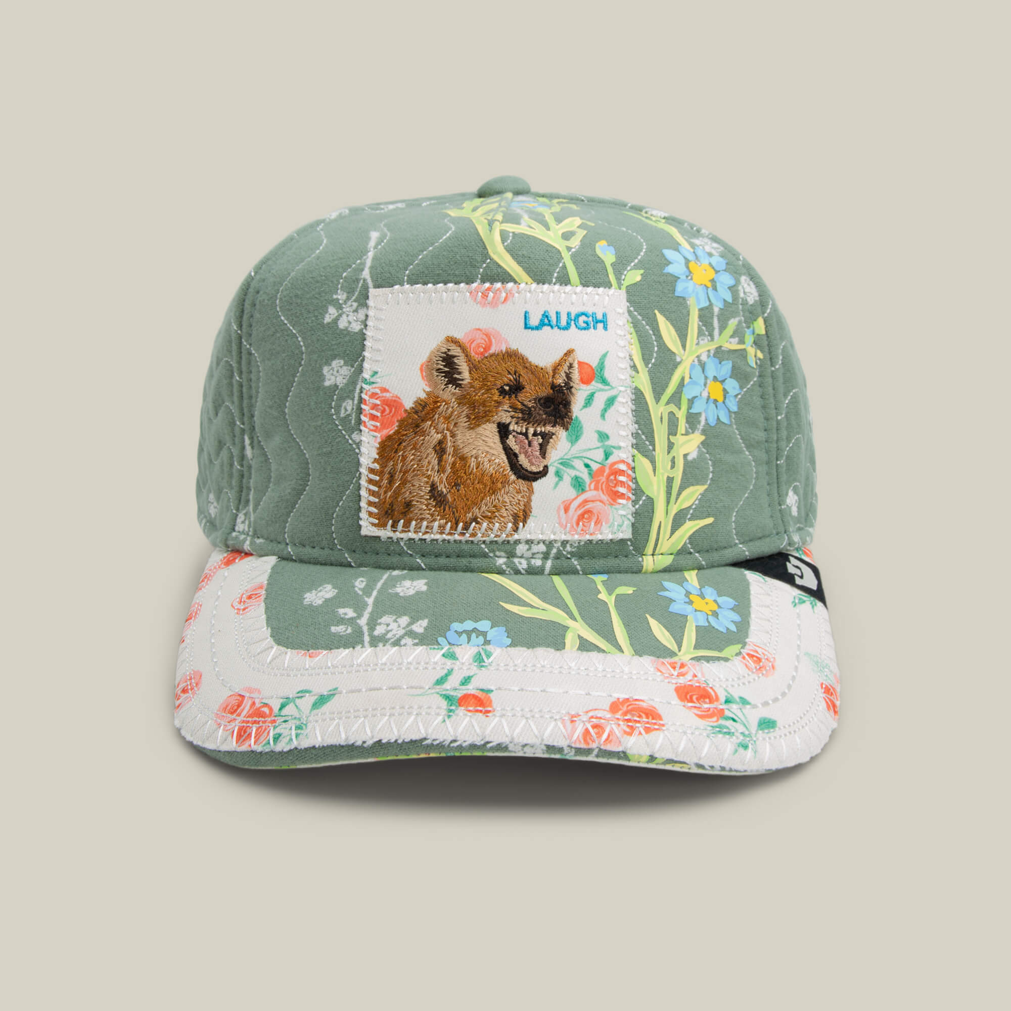 The Goorin Bros. Vol. 1 - Quiltbag: Laugh trucker hat in SHADE features patchwork patterns and a front embroidered LAUGH patch with a laughing hyena.