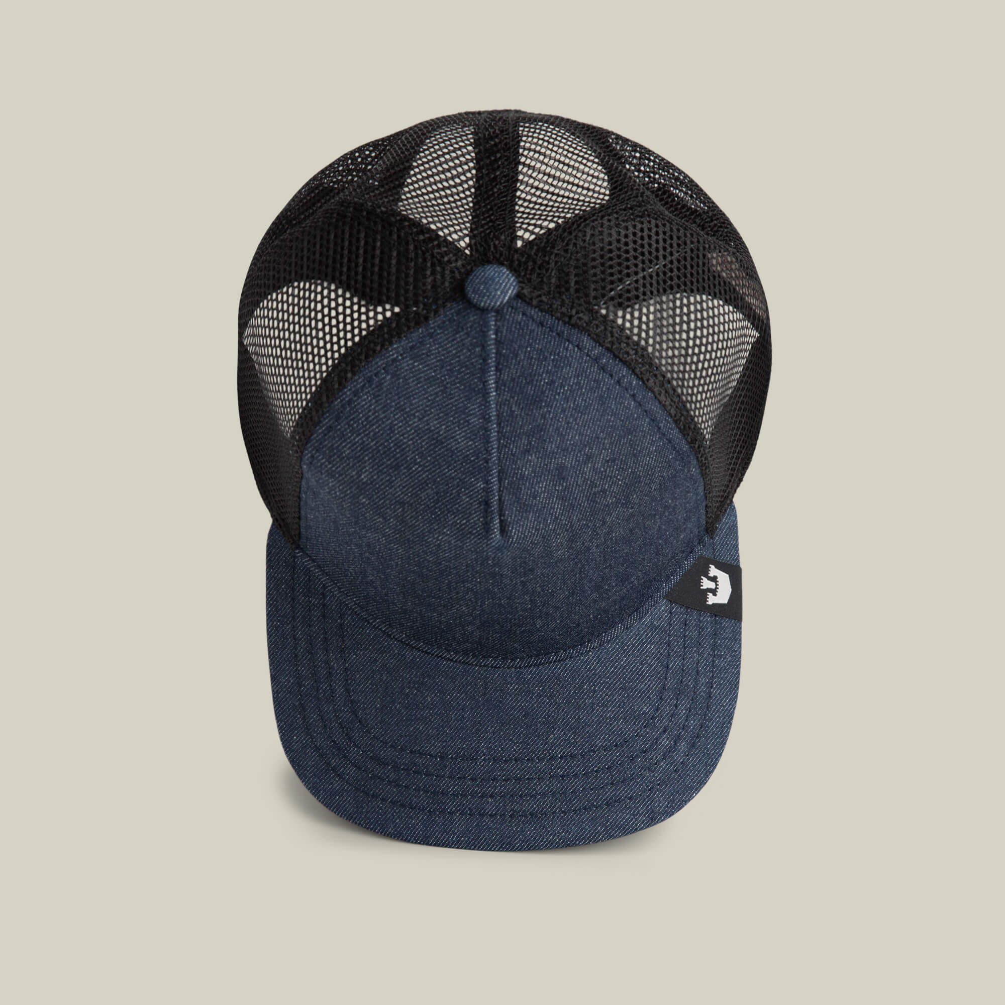 The Goorin Bros. Clean Denim Trucker hat, made in the USA, features a blue denim front, black mesh back, and a small black tag with a white logo on the brim. It's shown from above on a plain light background.