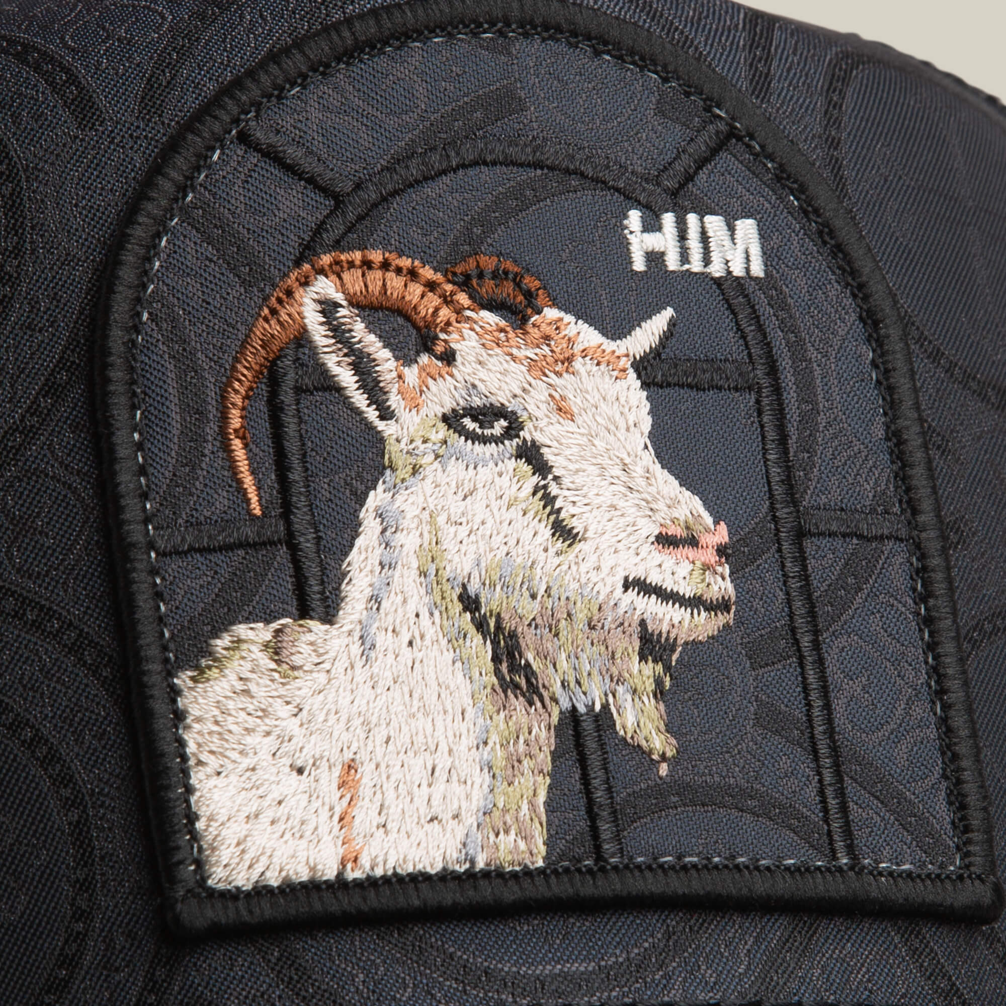 The Goorin Bros. Religulous - Hymn hat features a detailed embroidered goat patch with "HIM" above it, sewn onto a charcoal black cap for a bold statement.
