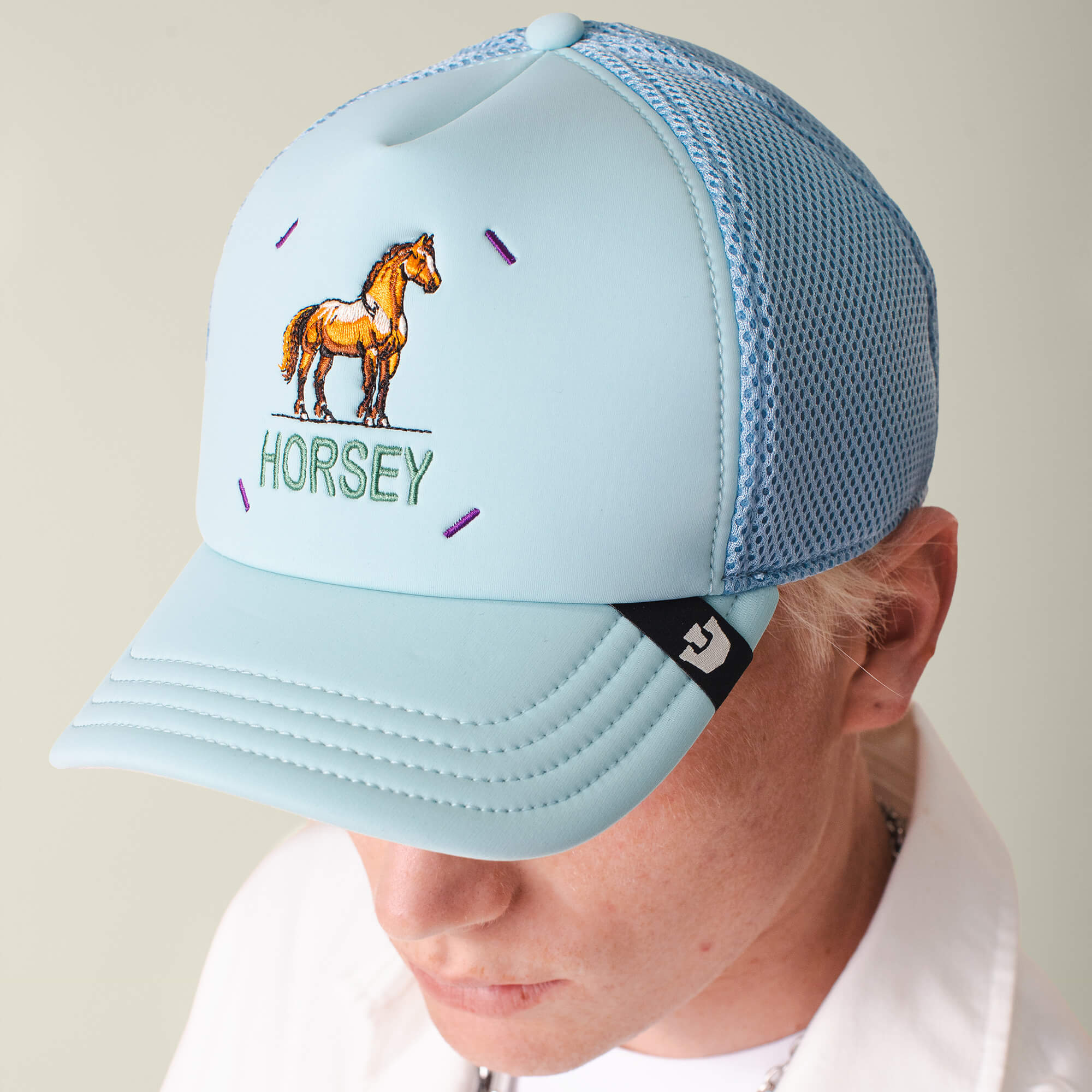 A person wears the Neo Farm - Horsey Horse cap by Goorin Bros., a light blue mesh hat featuring an embroidered horse and "HORSEY" text on the front, styled facing downward for a breathable, casual look.