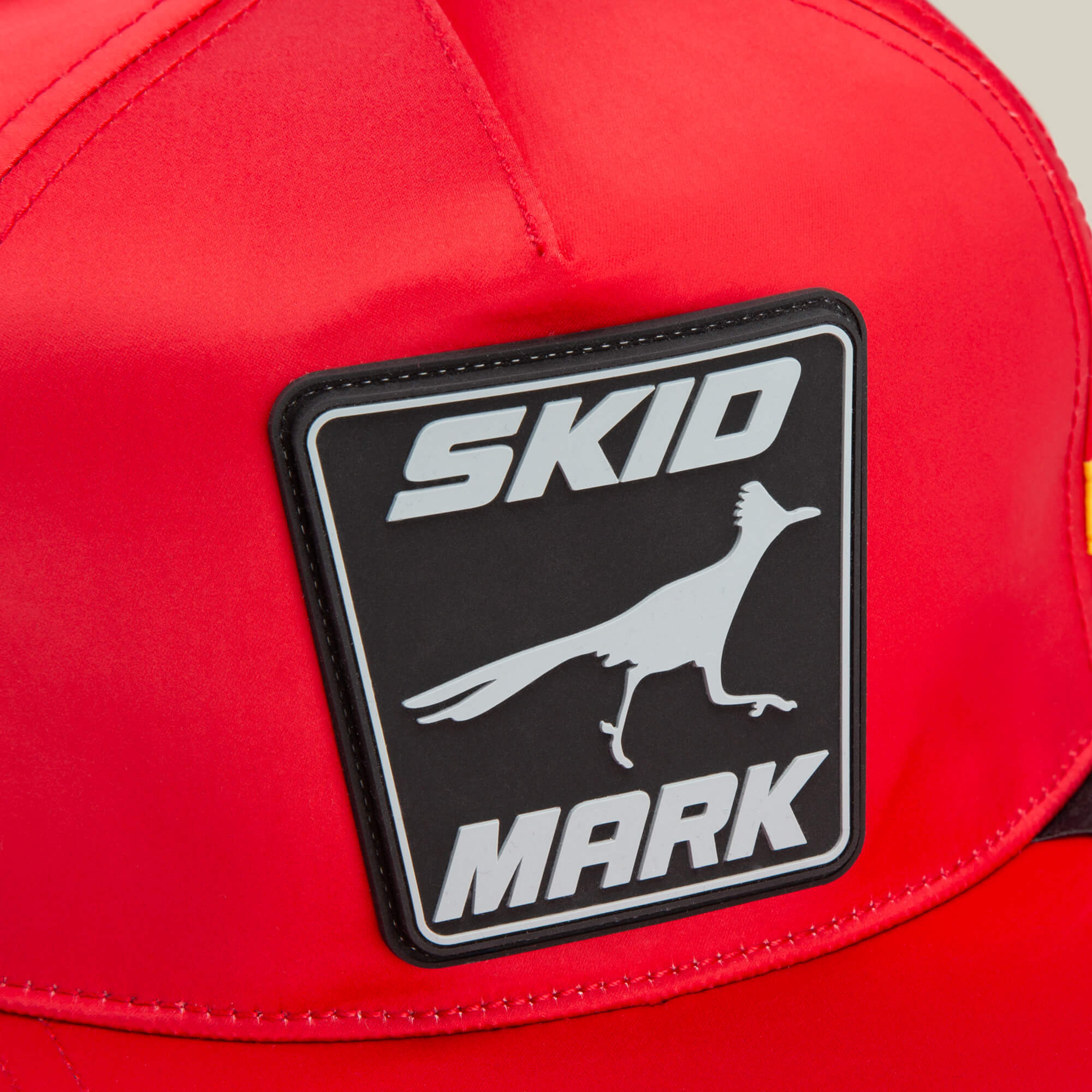 Close-up of the Goorin Bros. Pole Position - Skid Mark red cap, featuring a black and white patch with "SKID MARK" and a running bird, evoking roadrunner speed.