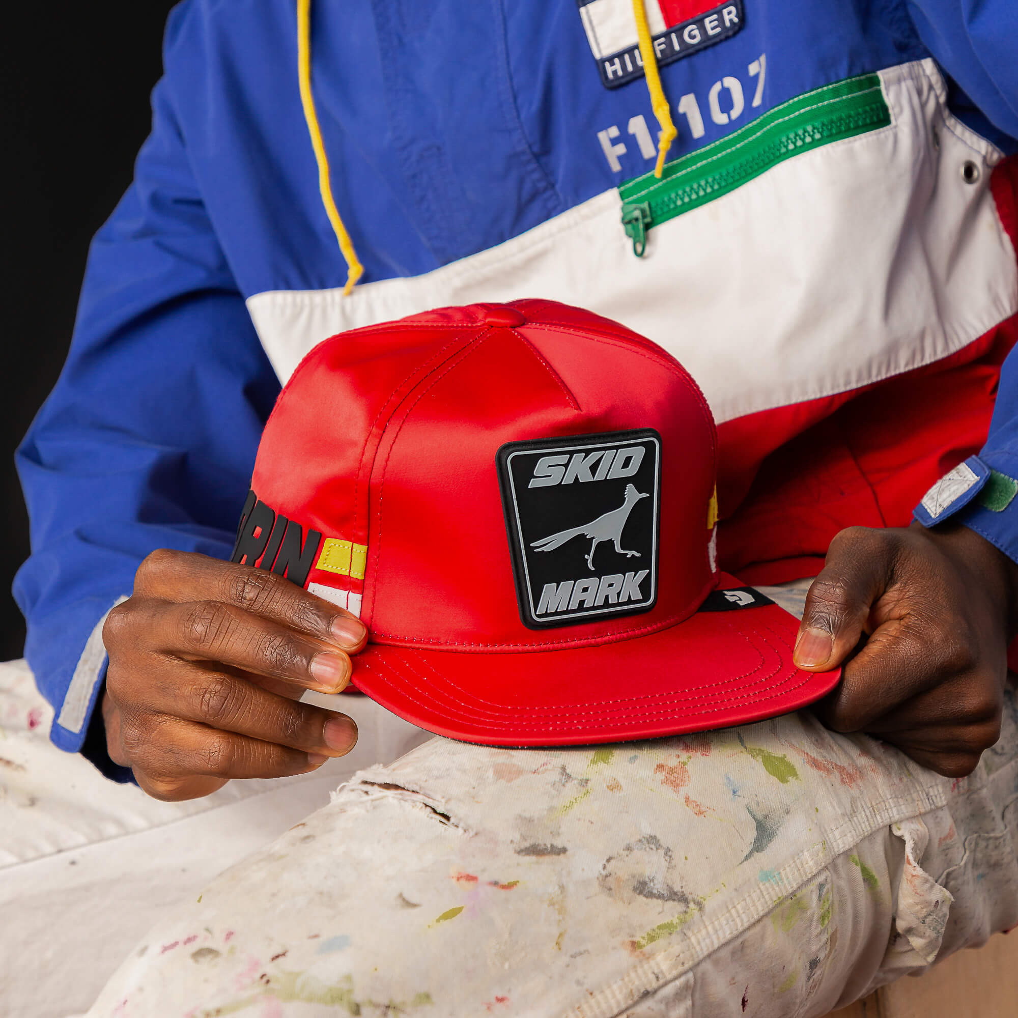 Wearing a colorful jacket and paint-splattered pants, someone shows off Goorin Bros.’ Pole Position - Skid Mark cap with a SKID MARK patch and bold black-and-white graphic, channeling roadrunner speed in standout street style.