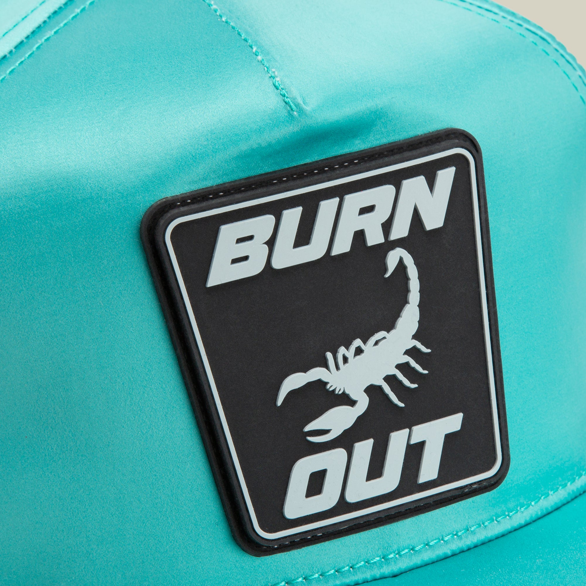 Close-up of the Goorin Bros. Pole Position - Road Kill teal racing cap, featuring a black patch with "BURN OUT" and a scorpion image.
