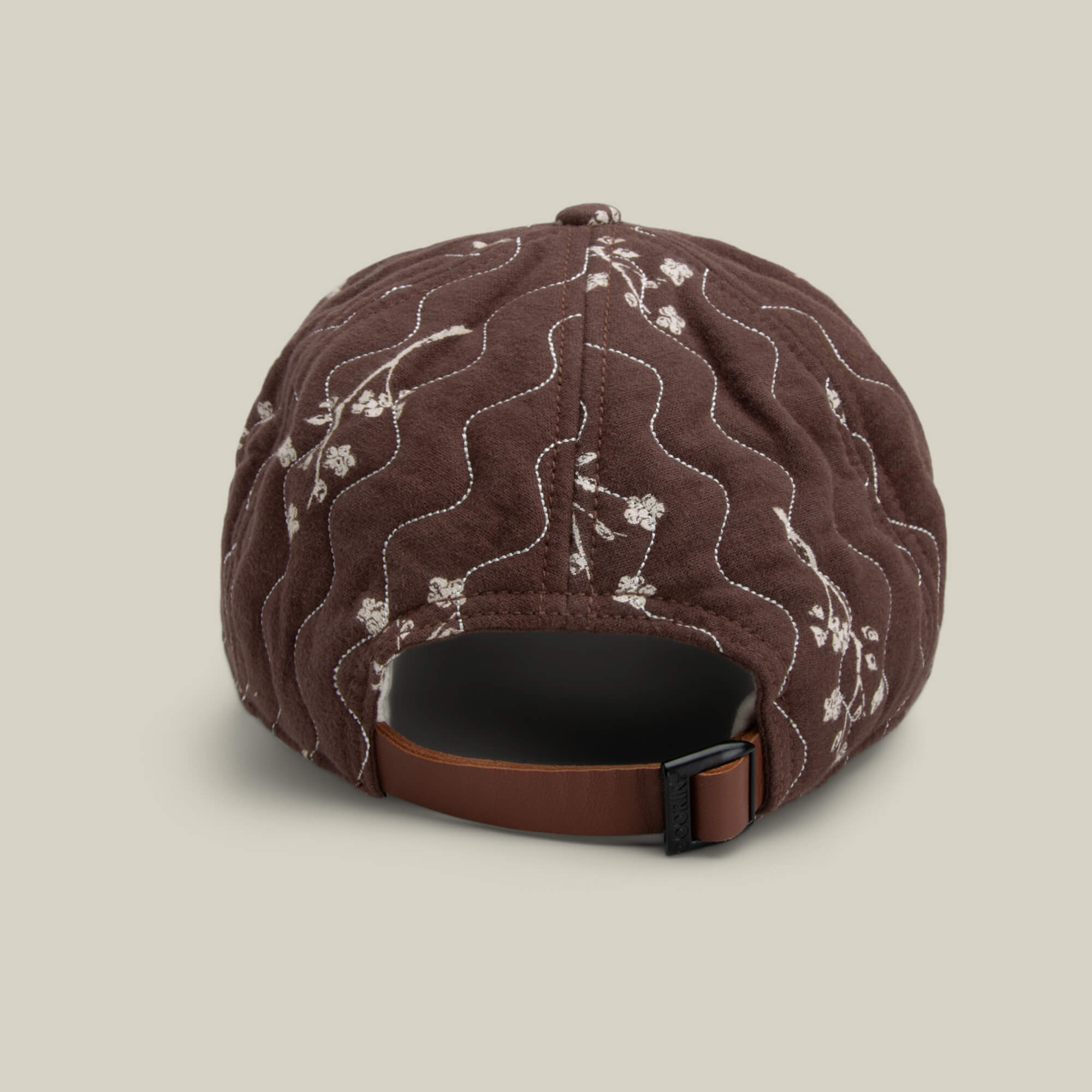 The Goorin Bros. Vol. 1 - Quiltbag: Love cap is shown from the back in chocolate brown with white floral embroidery and an adjustable brown strap with a black buckle.