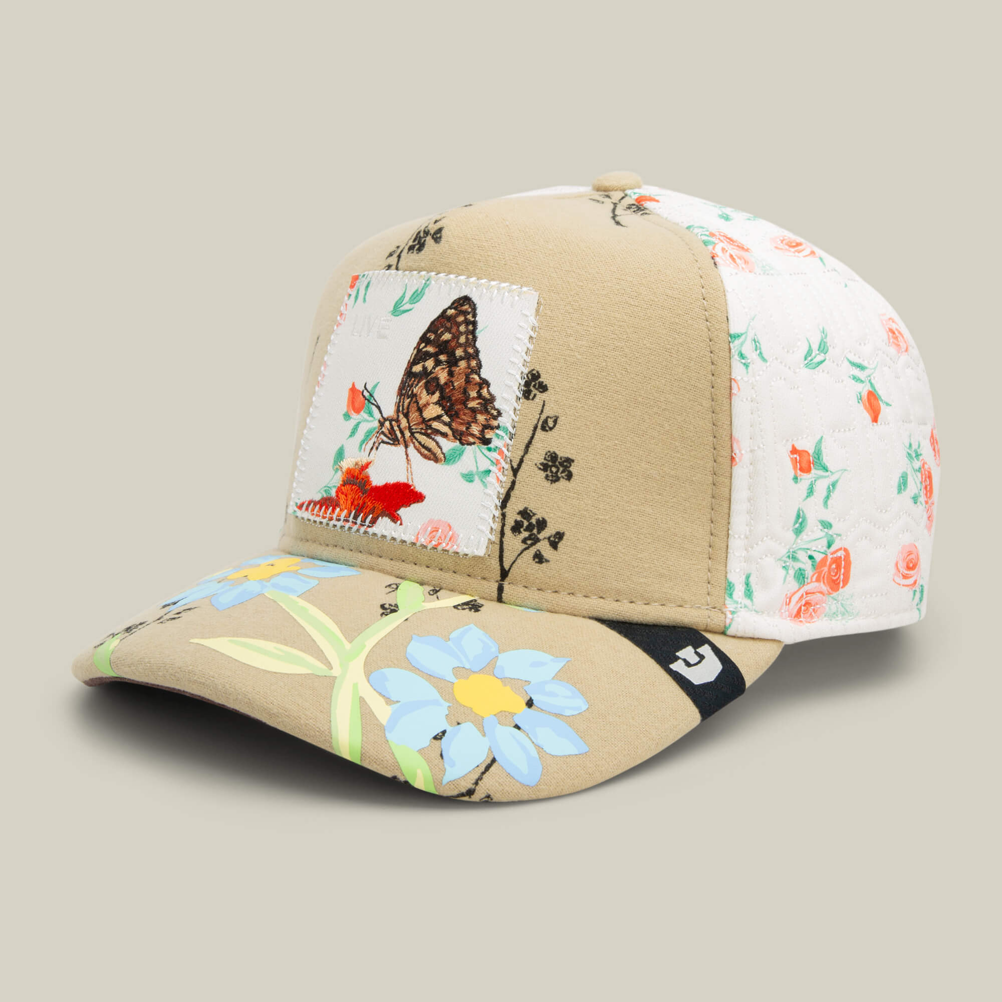 The Goorin Bros. Vol. 1 - Quiltbag: Live is a beige and white OG Trucker hat with floral embroidery, a blue flower on the brim, and a butterfly patch with red flowers on the front.