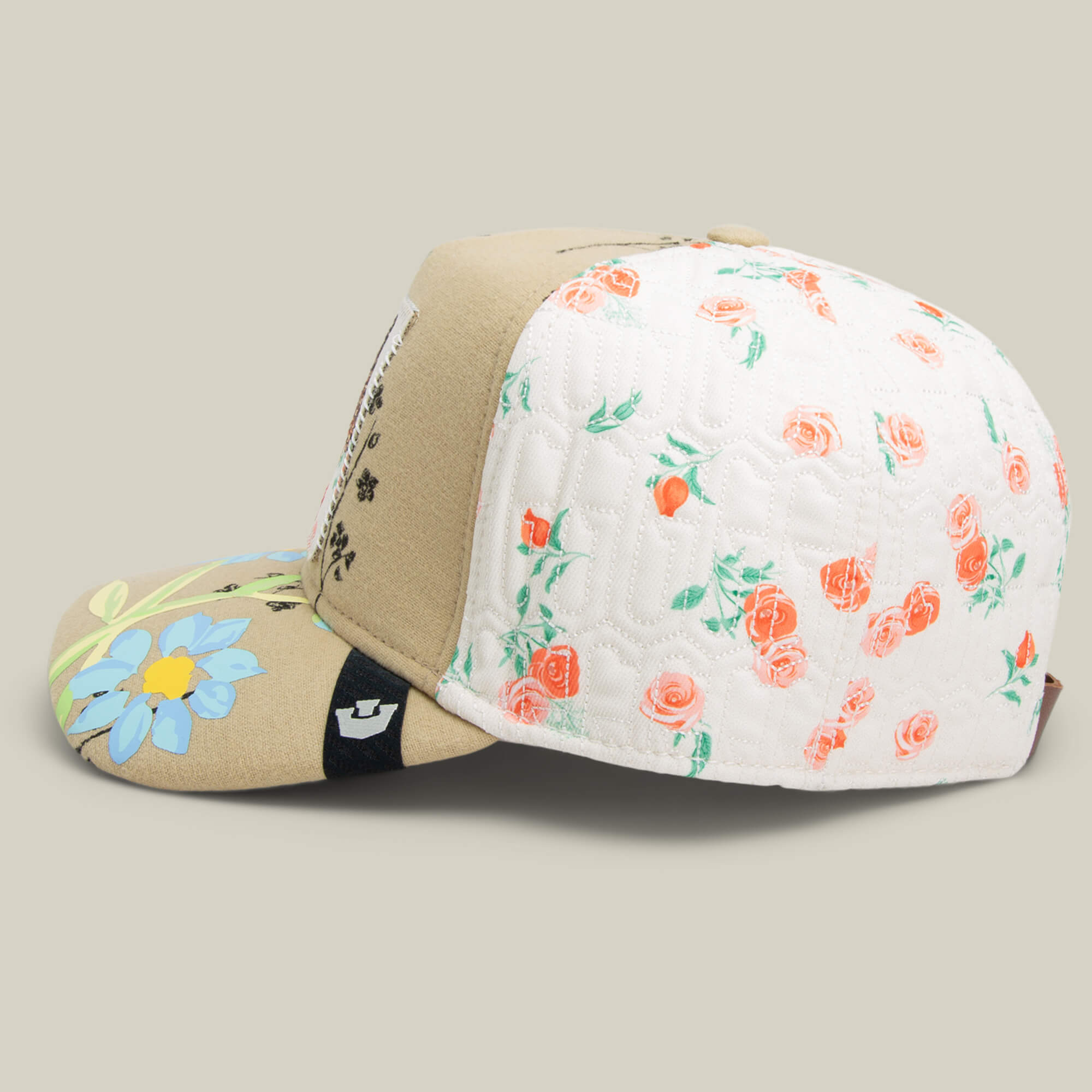 The Goorin Bros. Vol. 1 - Quiltbag: Live is a tan and white OG Trucker hat with a quilted floral pattern, pink rose accents, a bold blue daisy on the brim, and detailed floral embroidery for extra charm.