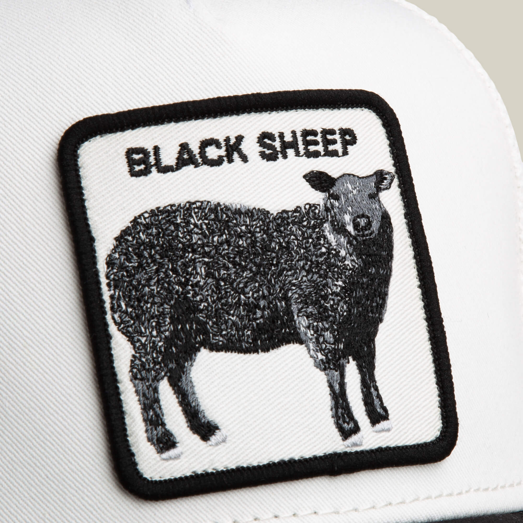 The Suede Sheep hat by Goorin Bros. is white with a black sheep patch in a rectangular design and "BLACK SHEEP" embroidered above it, all in classic black and white.