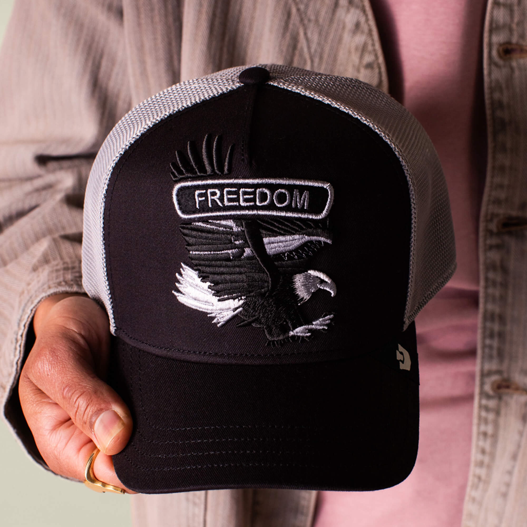A person holds the Goorin Bros. Classic Rocker - Freedom trucker hat, featuring a black and white design with a bald eagle patch and "FREEDOM" embroidered on the front for a bold, vintage rocker vibe.