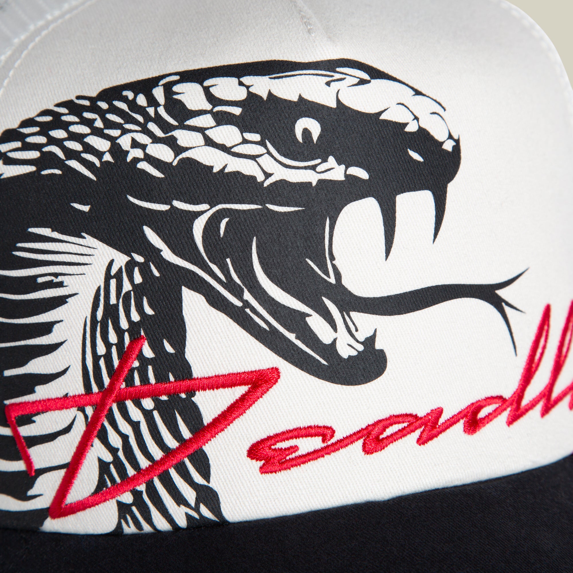 Close-up of the Goorin Bros. Outside the Lines Snake trucker hat in cream and black, featuring a black and white cobra illustration and partially visible red "Deadly" script on the front.
