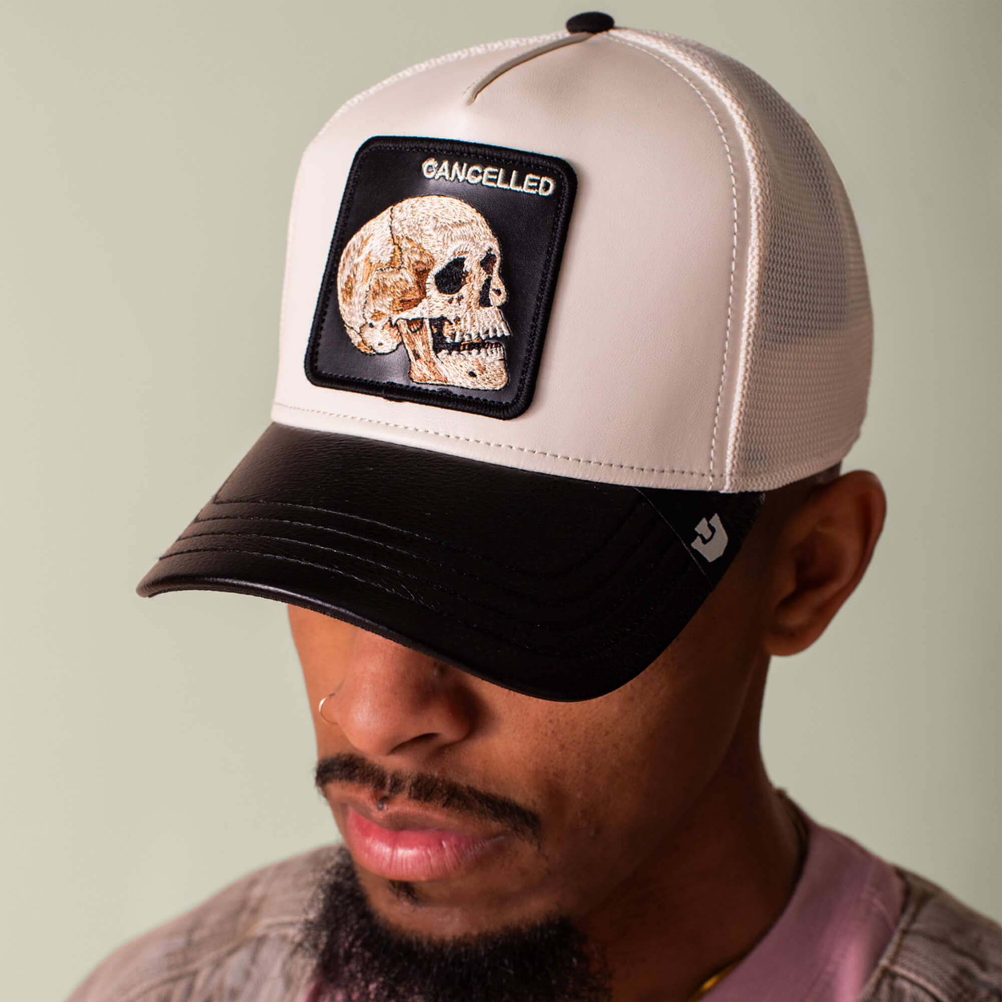 A person sports the Goorin Bros. Faux Leather Skull trucker hat in black and white, featuring a skull patch and CANCELLED embroidery for a bold, neutral-toned statement.