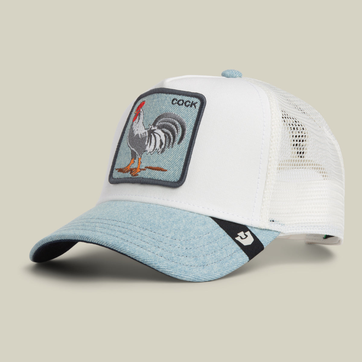 The Goorin Bros. Denim Rooster is a white and light blue denim trucker hat featuring a rooster patch with the word “COCK.” This trucker hat has a mesh back and a curved brim.