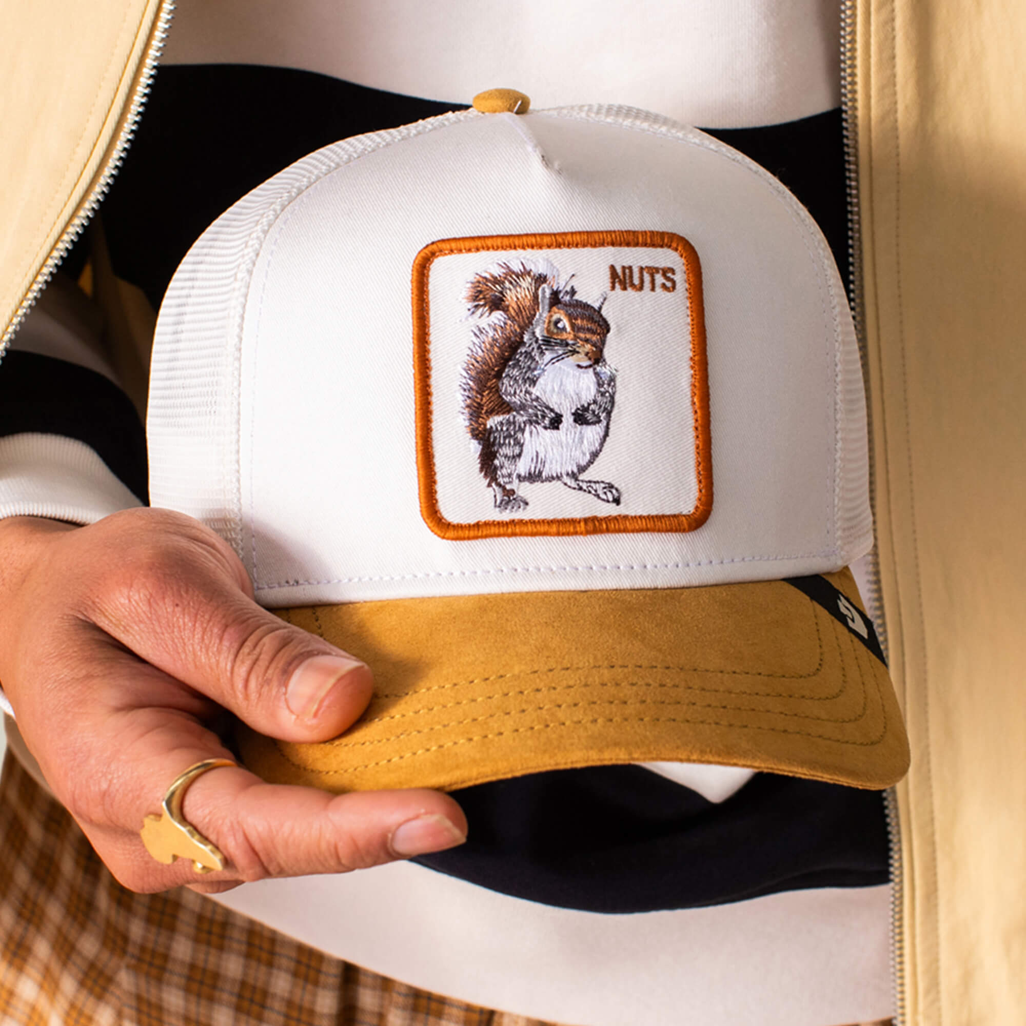 A person holds the Goorin Bros. Suede Squirrel hat, which has a white crown, yellow details, and an embroidered squirrel with the word NUTS.
