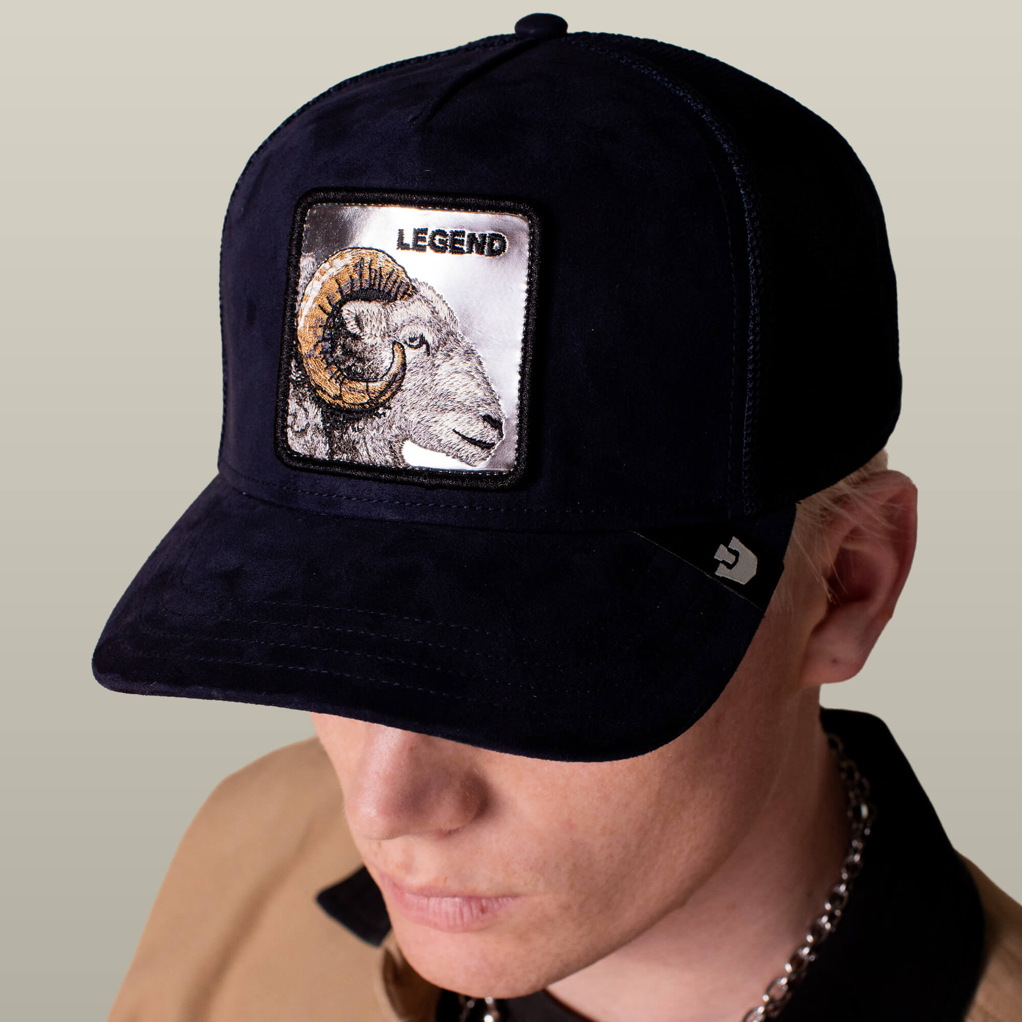 Person wearing the Goorin Bros. Silver Legend trucker cap, featuring a ram patch and "LEGEND" embroidered above it. The brim partly covers their face.