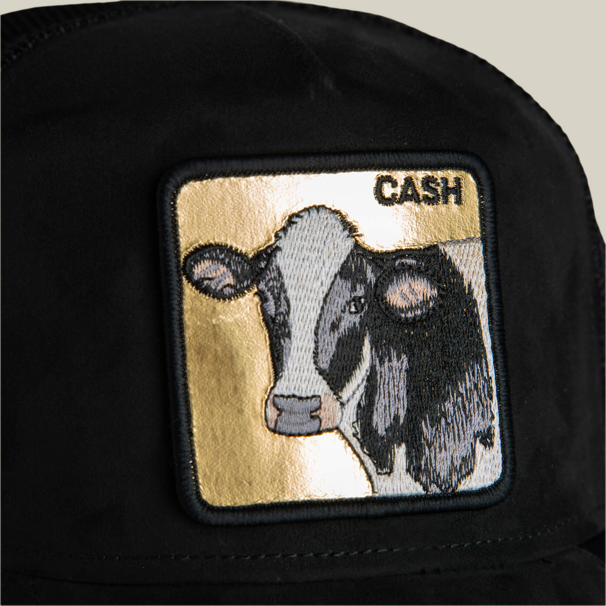 Close-up of the Goorin Bros. Golden Cow black suede hat with a rectangular patch showing an embroidered cow on a gold and white background and the word CASH in the top right corner.