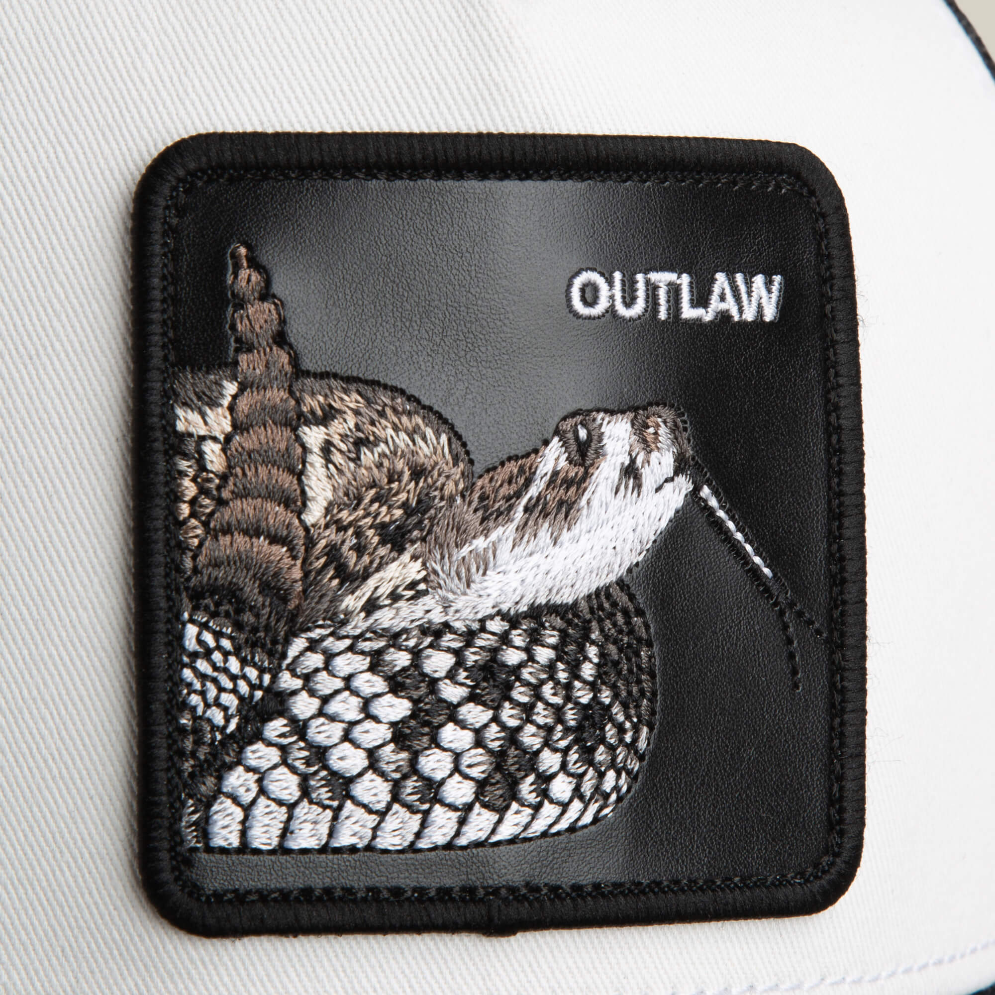 The Goorin Bros. Outlaw Trucker features a black rattlesnake patch with white "OUTLAW" embroidery, sewn on a white background—ideal for customizing your favorite trucker hat.