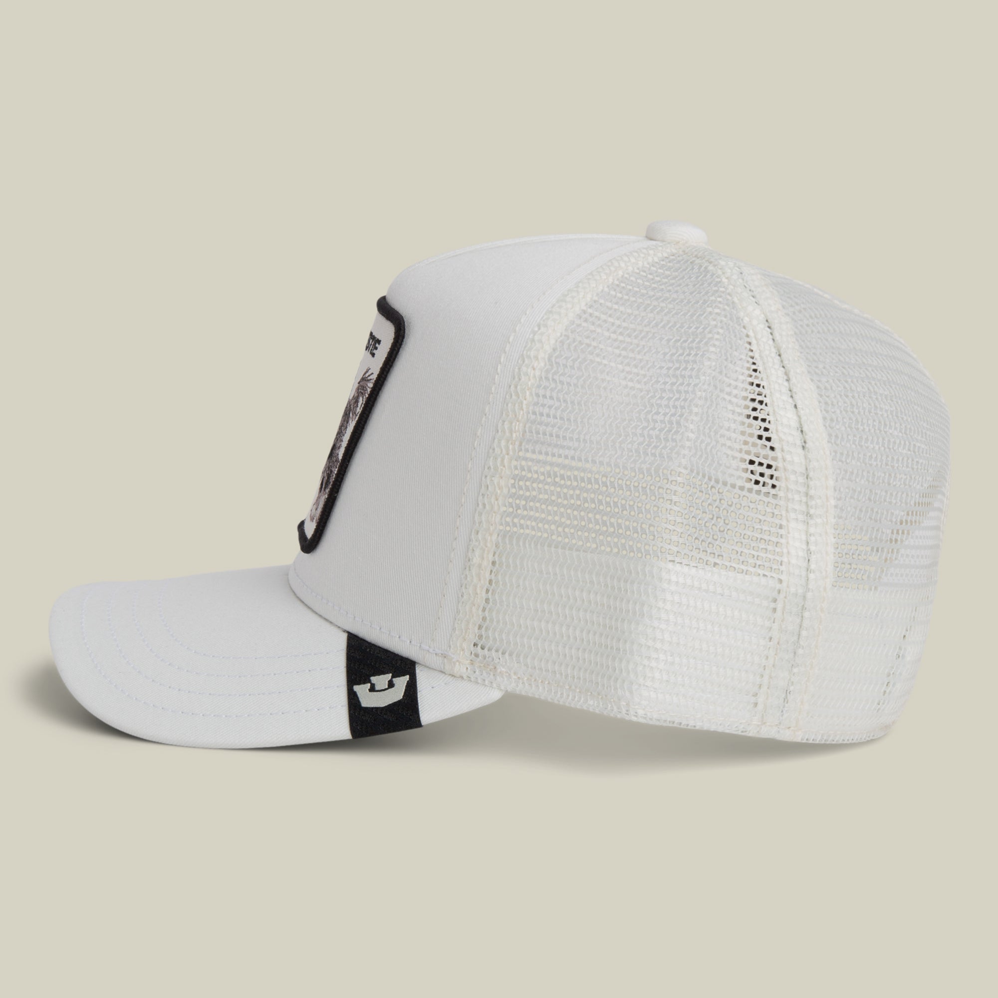 The Bestie Trucker by Goorin Bros. is a white mesh hat with a curved brim, seen from the side, featuring a black tag and a framed patch on the front panel.