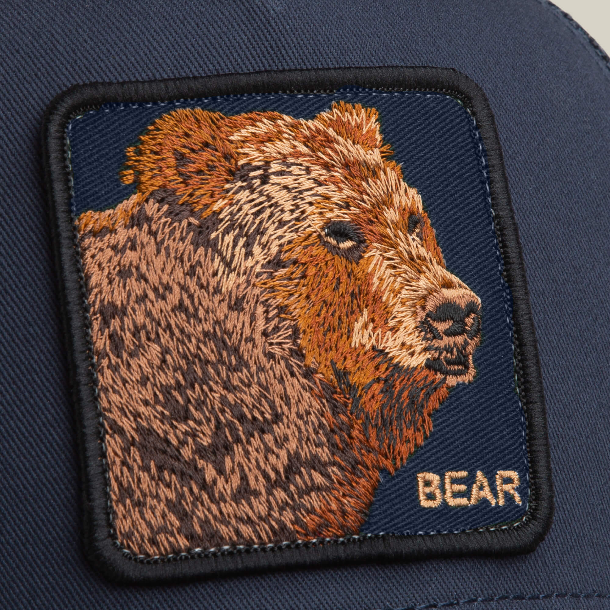 A close-up of the Bear Trucker by Goorin Bros., showing a detailed bear patch with "BEAR" in yellow embroidery—an ideal way to add character to your favorite navy trucker hat.