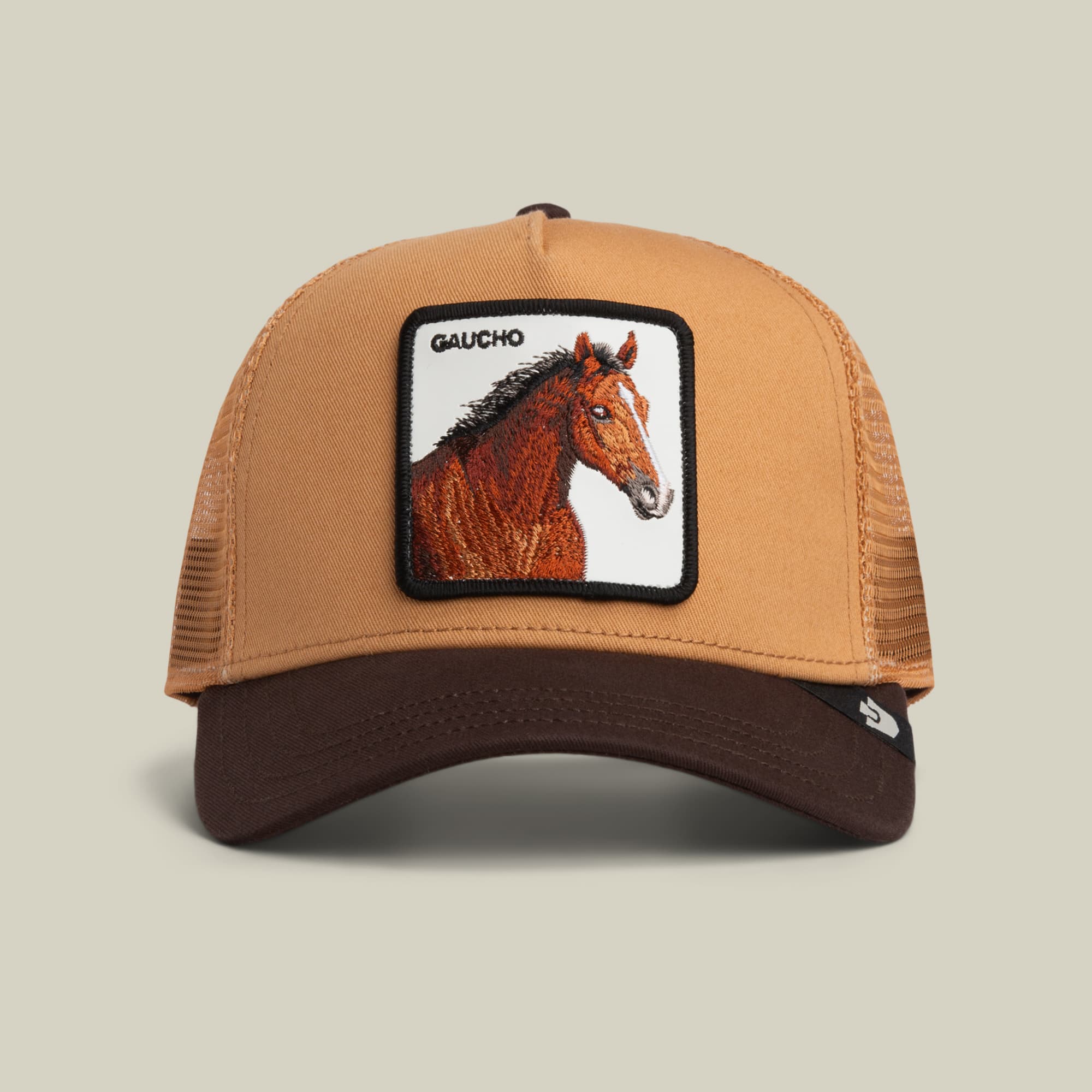 The Goorin Bros. Gaucho Trucker is a brown and tan trucker hat in an earthy colorway, featuring a leather patch with an embroidered horse and “GAUCHO” above it, displayed on a neutral background.