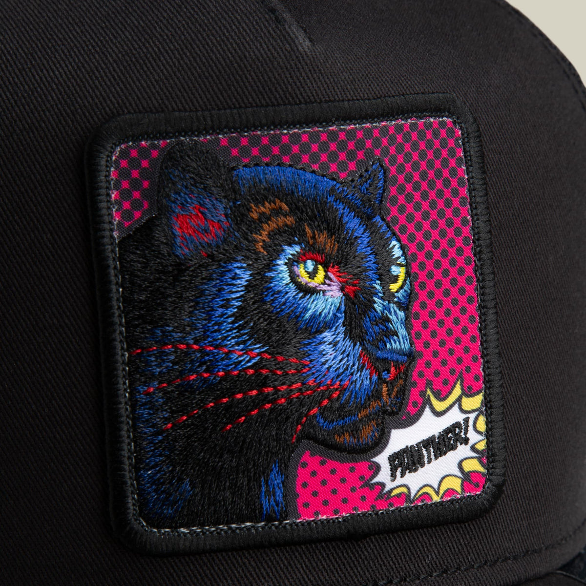 The Goorin Bros. POPArt - Panther trucker hat features a colorful embroidered panther patch with blue, orange, and red details on a magenta dotted background, set on a black trucker cap.