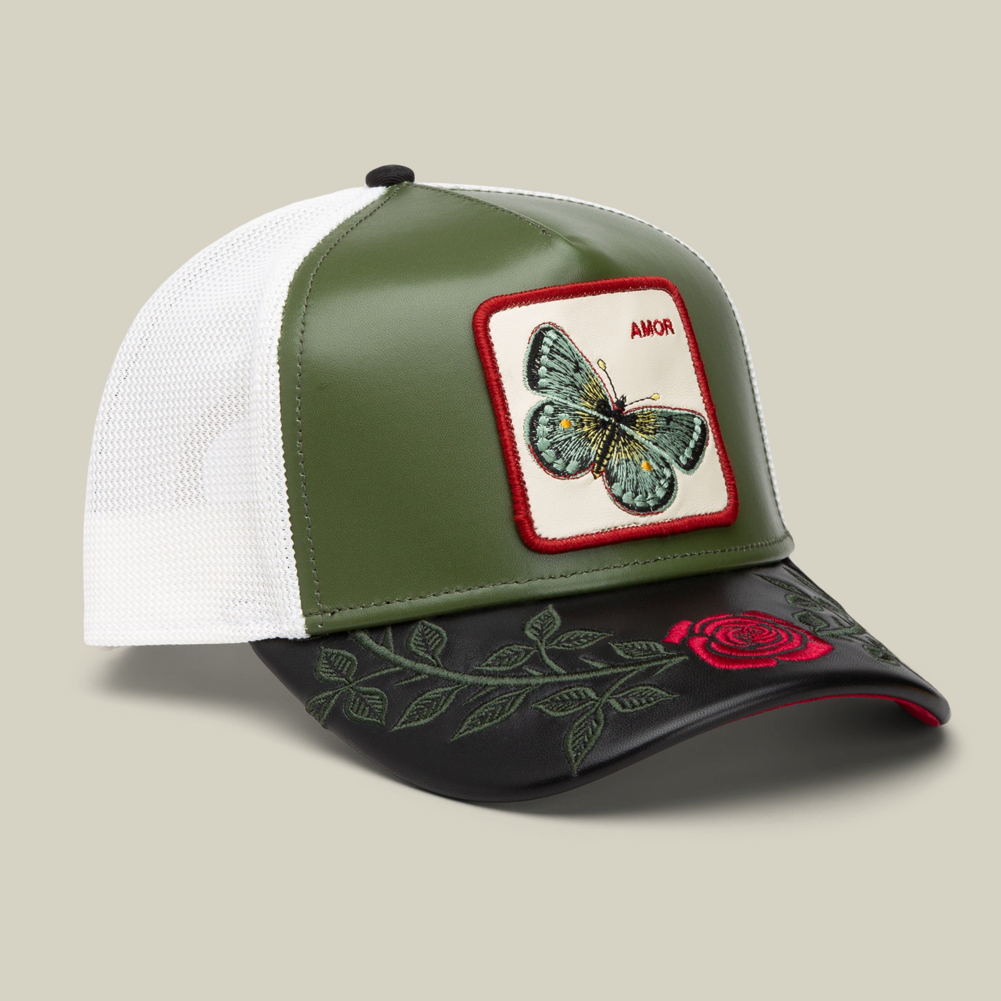 The Amor trucker hat by Goorin Bros. features green and white panels, a butterfly patch labeled AMOR, a black brim embroidered with a red rose and green leaves—ideal to pair with your favorite AMOR jewelry.