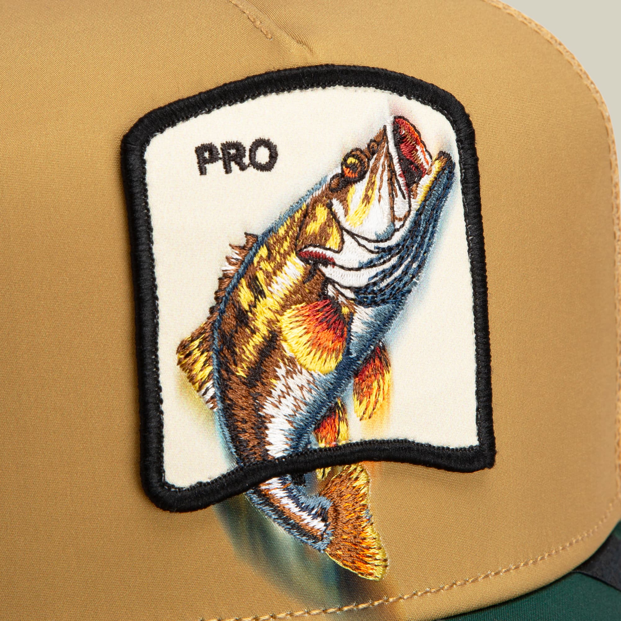 The Goorin Bros. Migration Pro trucker hat features a tan canvas front with an embroidered fish patch and "PRO" text, displayed against a neutral studio background.
