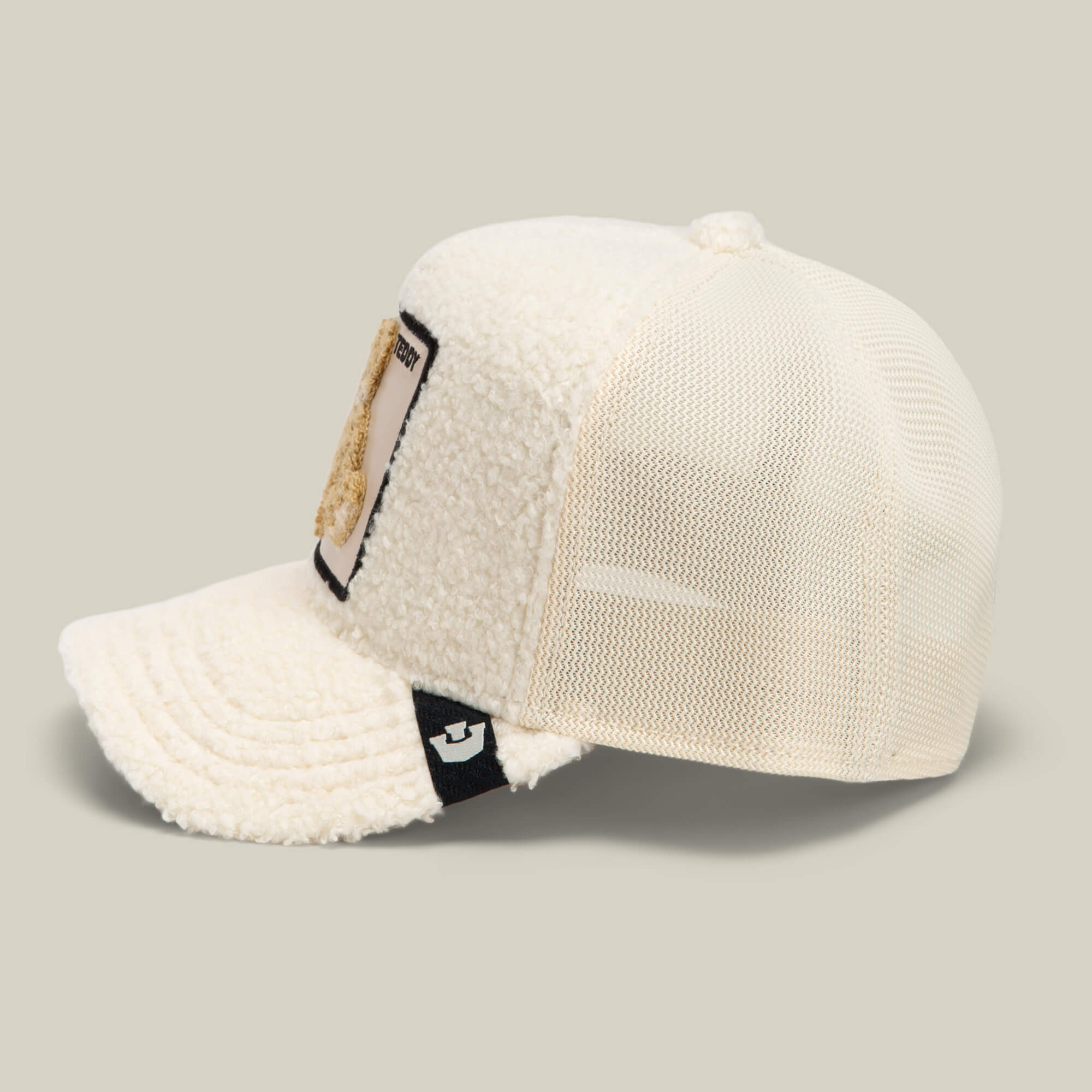 The Double Stuffed - Teddy by Goorin Bros. is a cream sherpa trucker hat featuring a mesh back, textured fleece front panel, a rectangular teddy patch on the front, and a small black tag on the side.