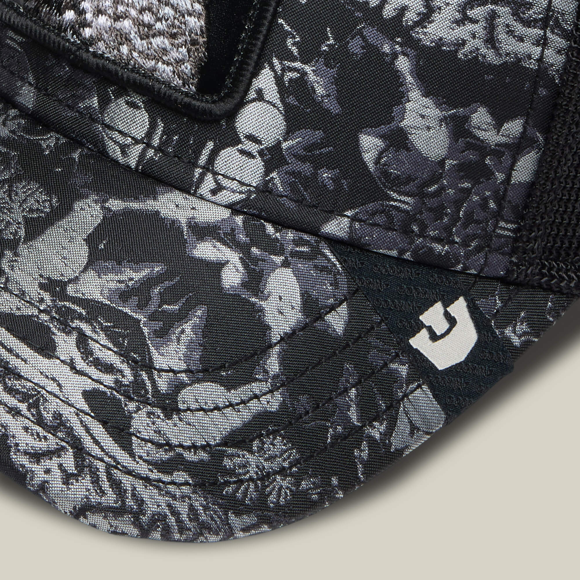 Close-up of the Goorin Bros. "Gray Matter" cap, black and gray with koi fish and aquatic plants, intricate like gray matter patterns, and a small white logo on the brim.