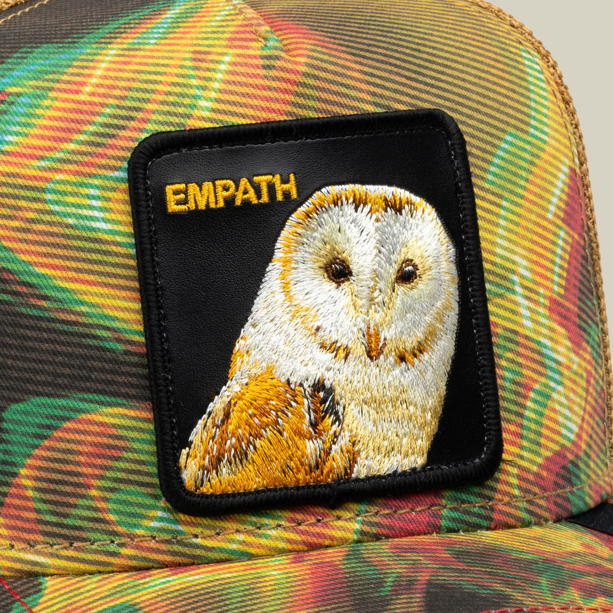 The Goorin Bros. Androids Dream trucker hat features a colorful rainbow striped fabric in yellow, green, and orange with an embroidered owl patch labeled "EMPATH" on the front.