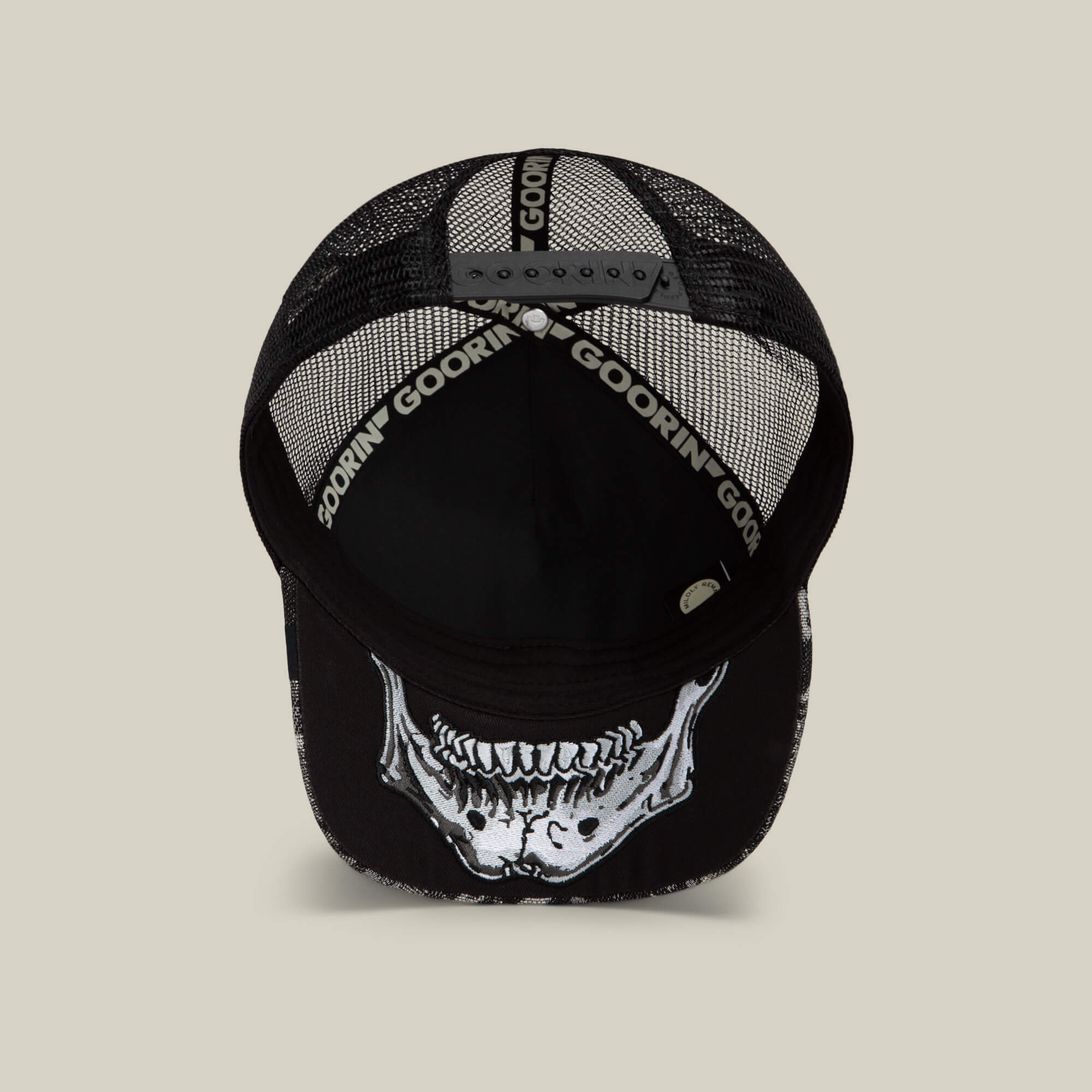 The Goorin Bros. Bone Head Unalive trucker hat, shown from above, features a black mesh back for breathable, all-day comfort and style. An open adjustable strap ensures a customizable fit, while a striking white skeleton jaw graphic decorates the underside of the brim.