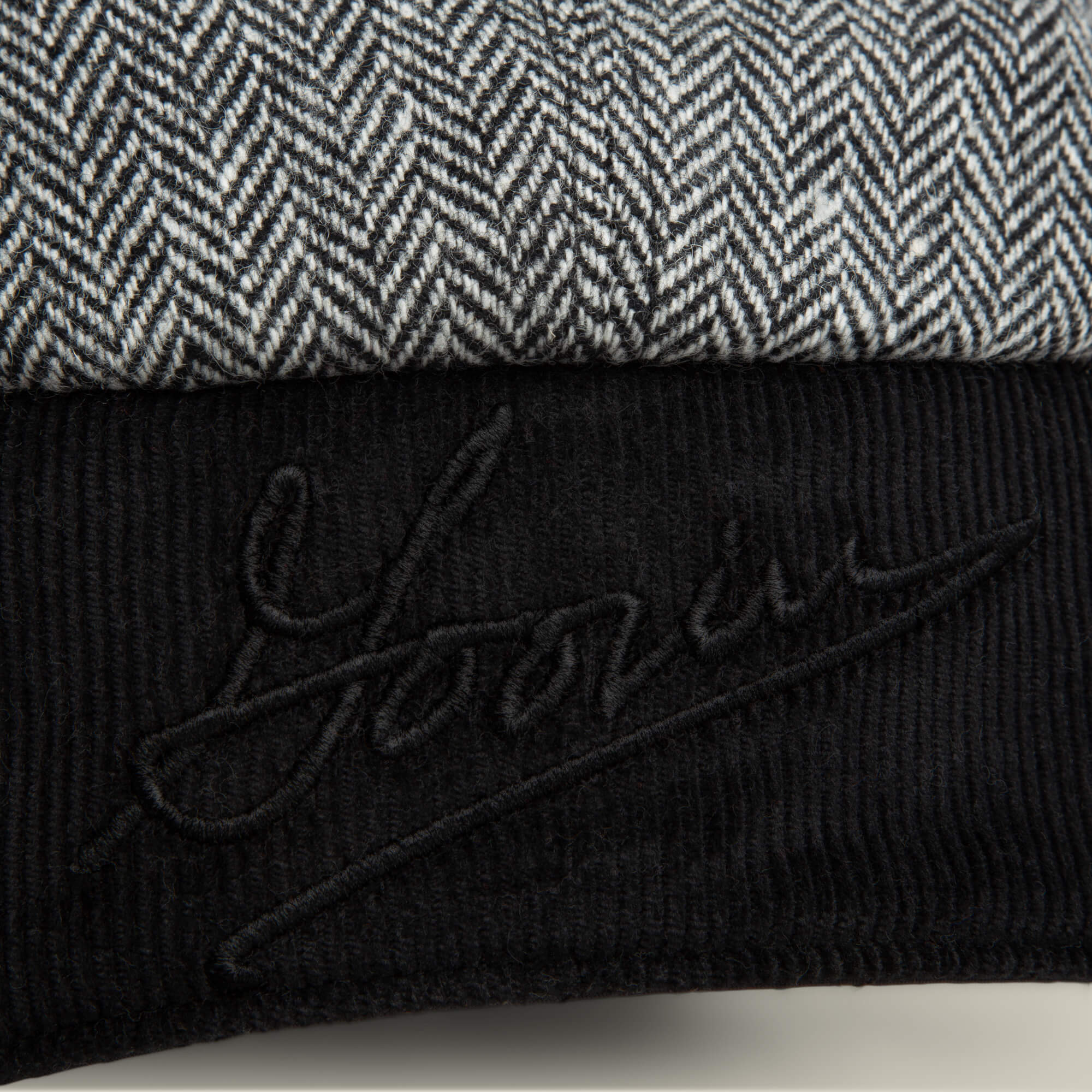 A close-up of the Goorin Bros. Frazier Lake hat, showing gray and white herringbone fabric with ear flaps and a black corduroy section embroidered with "Yours.