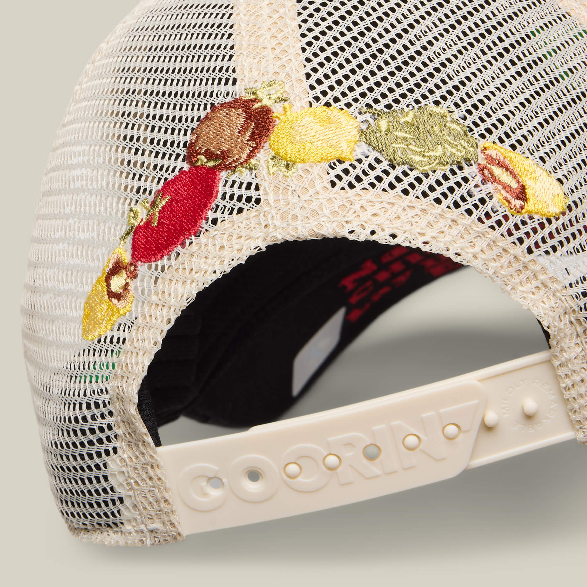 Close-up of the back of a mesh baseball cap by Goorin Bros., featuring multicolored embroidered fruit and an adjustable plastic strap labeled “GOORIN”—a playful tribute to home cookin’ with the Middle of No Where cap.