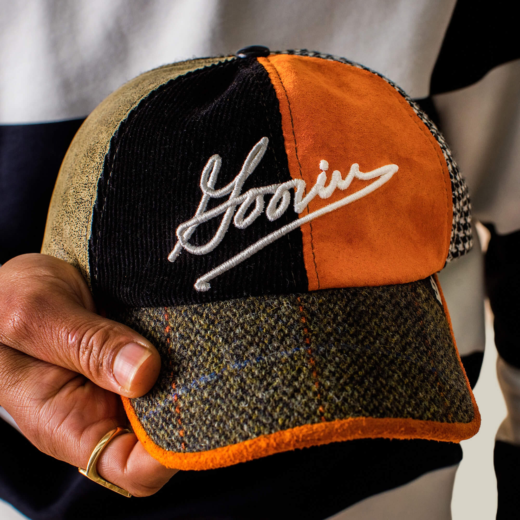 A hand holds the "South Bay" Papa cap by Goorin Bros., featuring Goorin Script on the front and bold orange, brown, and checkered textured panels for a standout style.