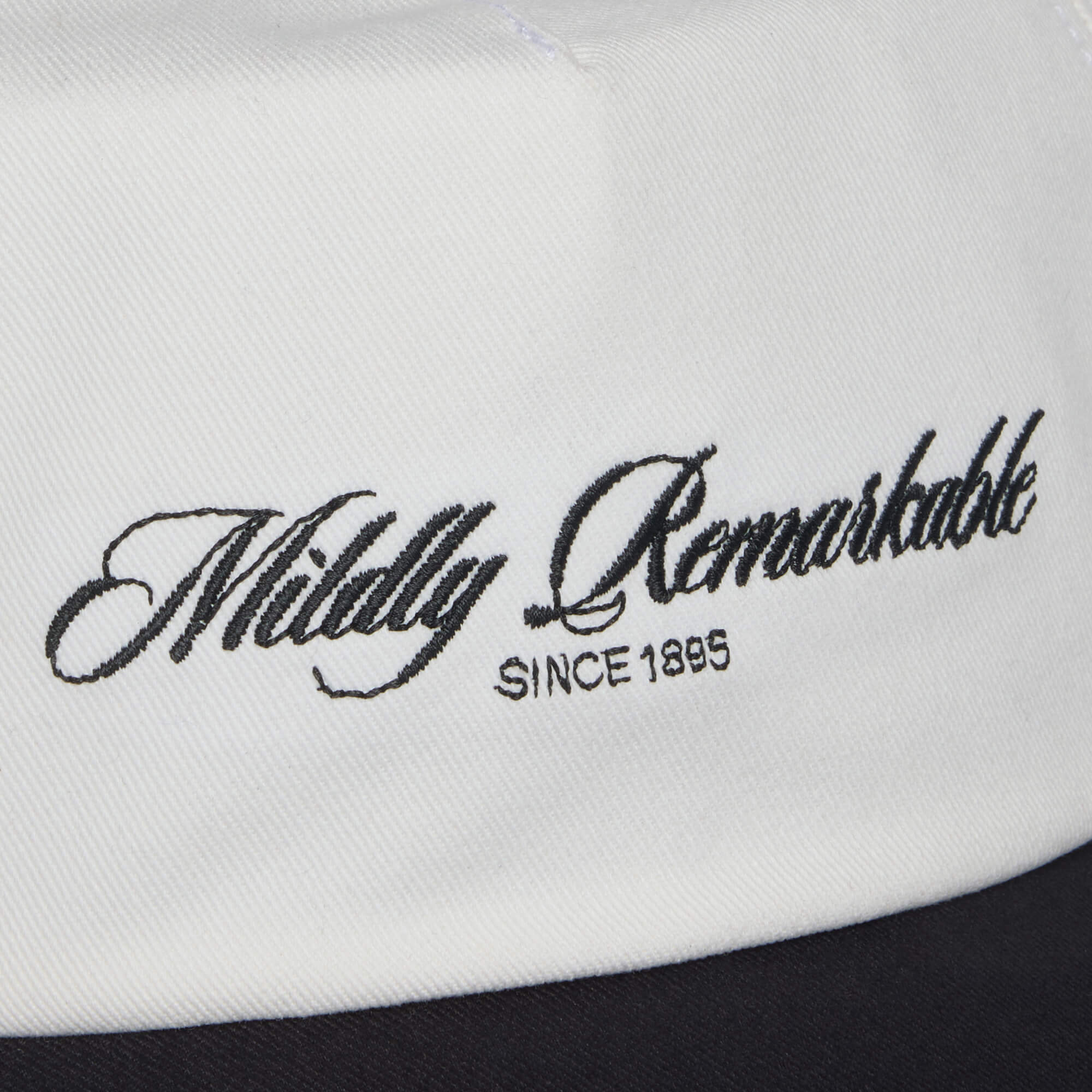 Close-up of white fabric featuring the Goorin Bros. Mildly Remarkable Script embroidery, "Mildly Remarkable SINCE 1895," evoking the timeless style of a classic Scrip hat.