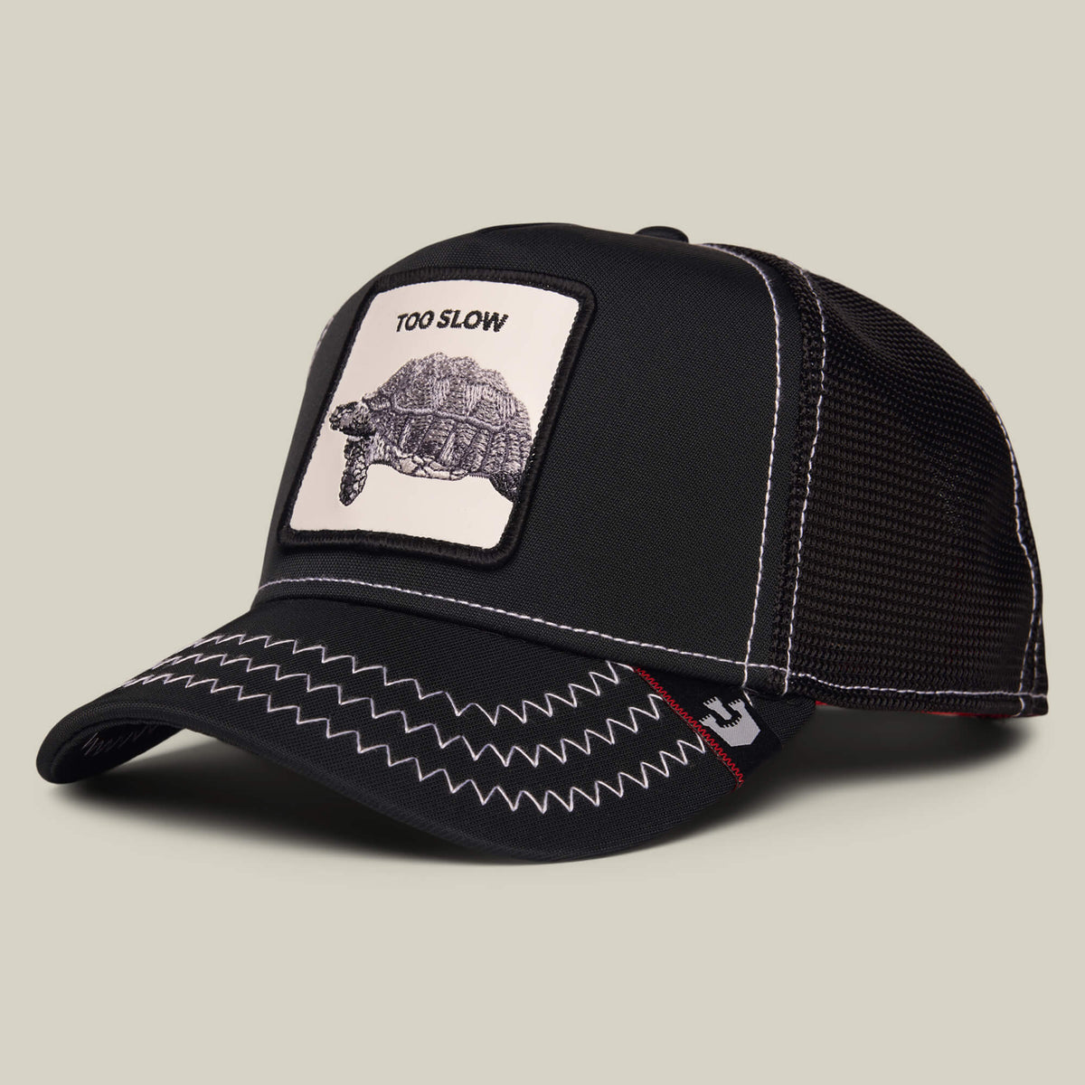 Black mesh-back cap from Goorin Bros. called "Down Low..." featuring a zigzag stitched brim and a front patch with a tortoise and the text TOO SLOW—a true badge of honor for those who embrace taking life at their own pace.