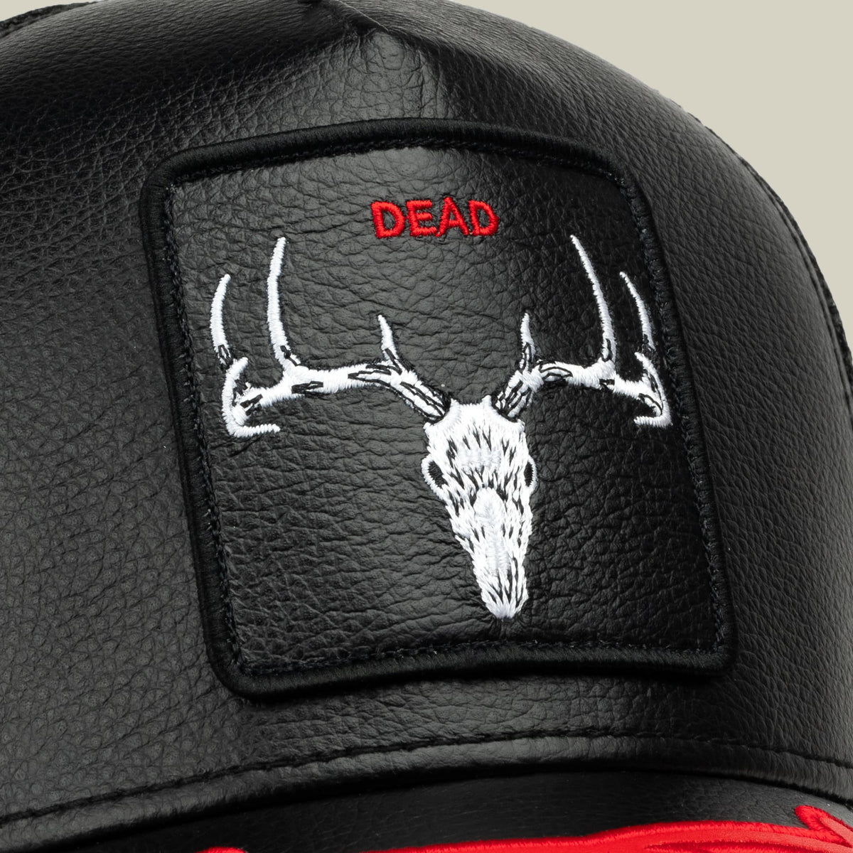 The Dead Bones Trucker by Goorin Bros. is a black leather trucker hat featuring an embroidered white deer skull with antlers and red "DEAD" text on a patch, displayed in a close-up studio shot.