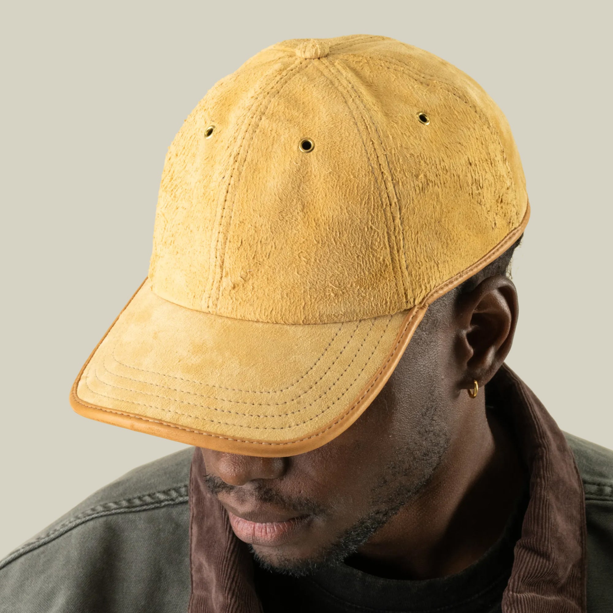 A person wearing the Goorin Bros. Steiner yellow suede papa cap with an adjustable plaid strap and a dark jacket, looking downward against a neutral background.