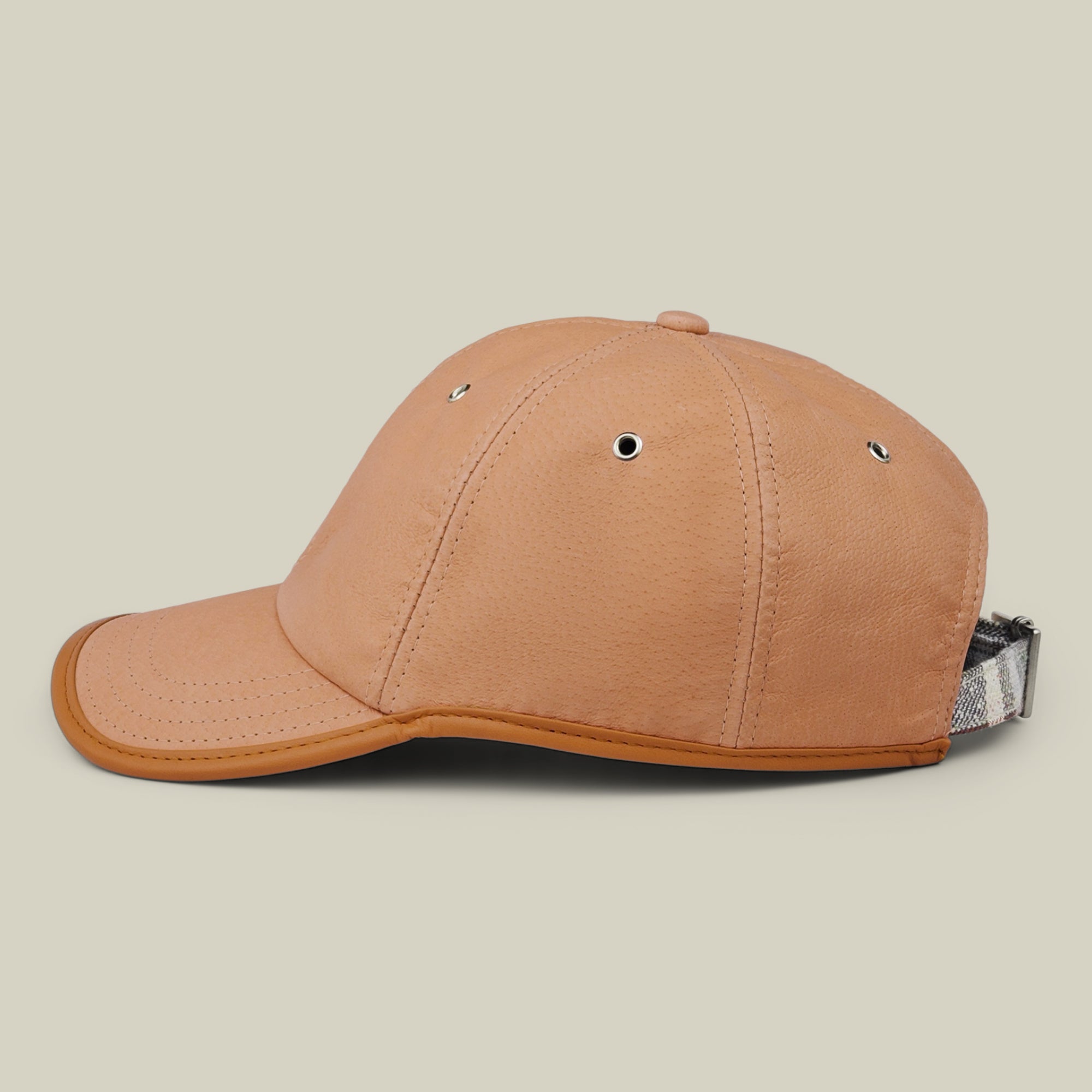 The Steiner by Goorin Bros. is a tan leather papa cap featuring silver eyelets and a gray plaid adjustable strap, displayed in profile against a neutral background.