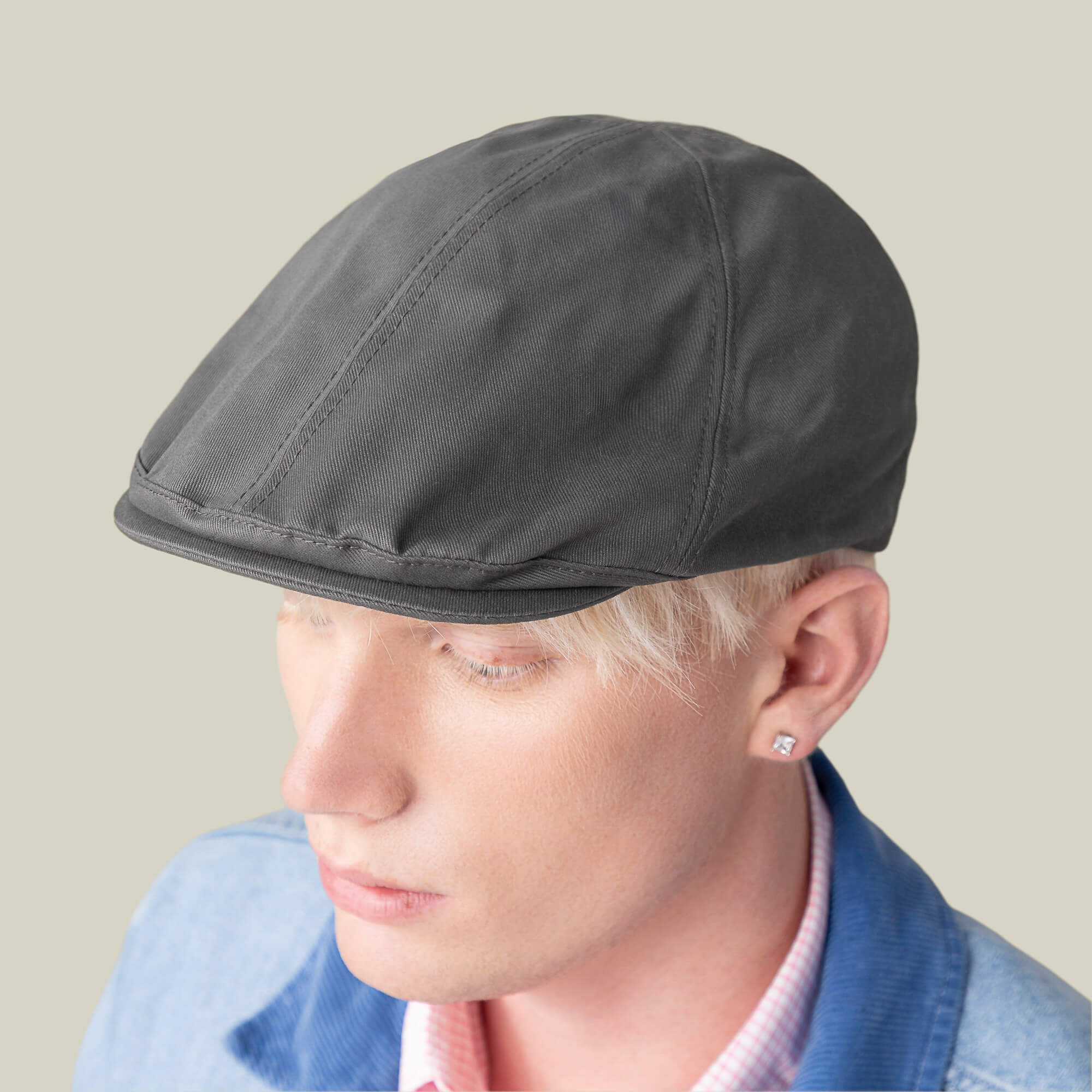 A person with short blonde hair and a stud earring wears the Goorin Bros. Murray Way gray flatcap, a light 100% cotton denim jacket, and a pink checkered shirt against a plain background.
