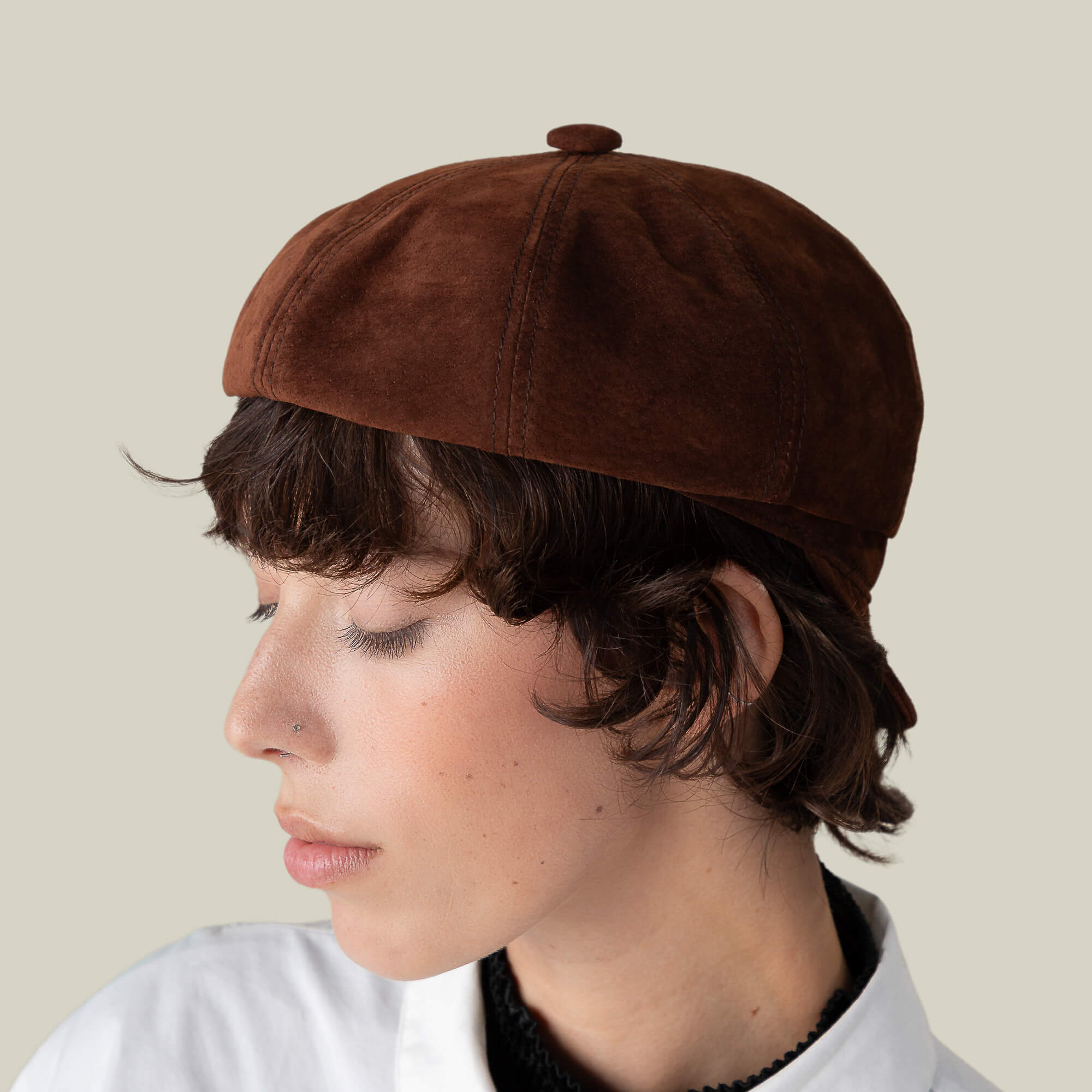 Person with short brown hair wears the Goorin Bros. Ruthy suede cabbie flatcap and a white collared shirt, facing left against a plain beige background.