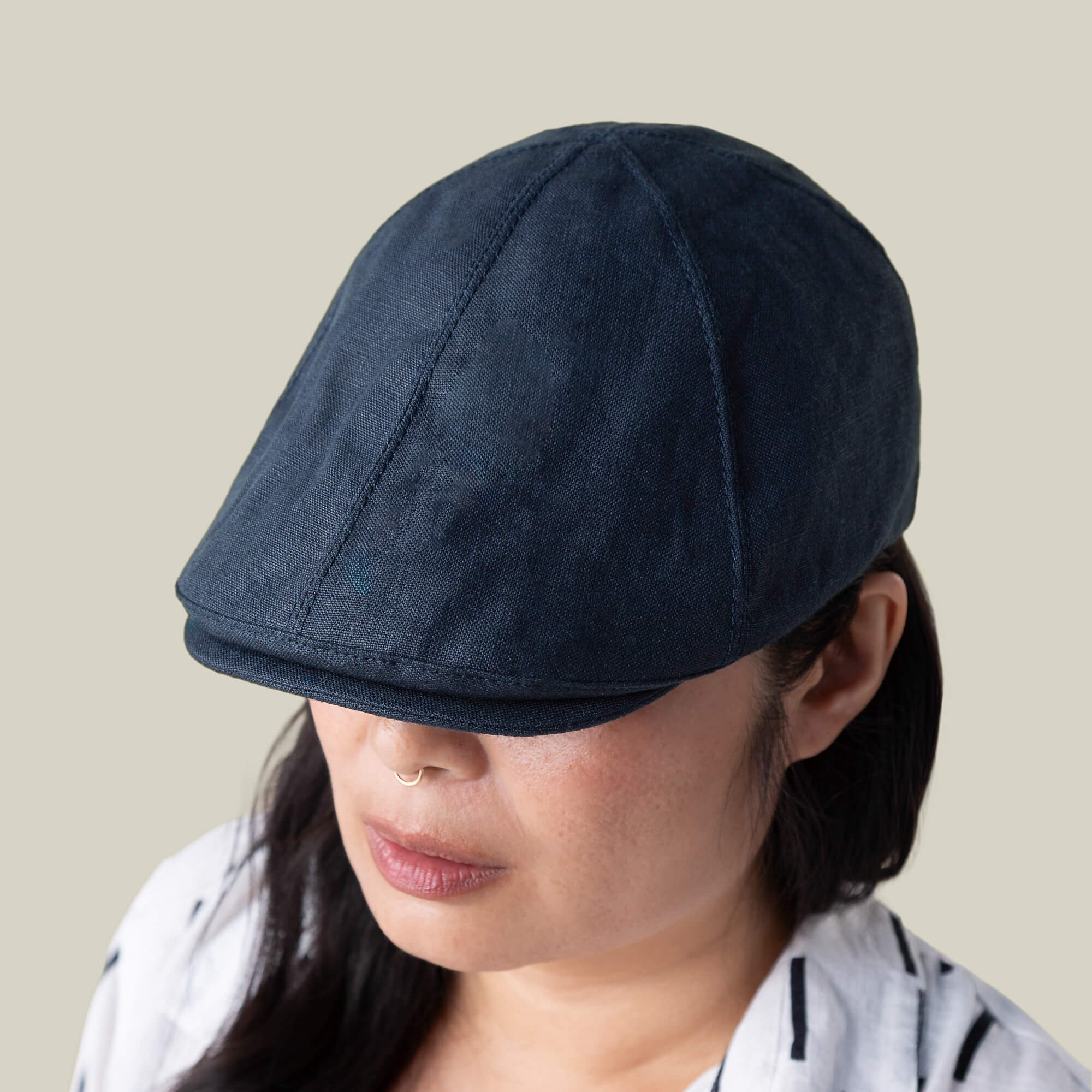 A person is seen from above wearing the Benjamin Paul dark blue six-panel hat by Goorin Bros. and a white shirt with black stripes, set against a plain background.