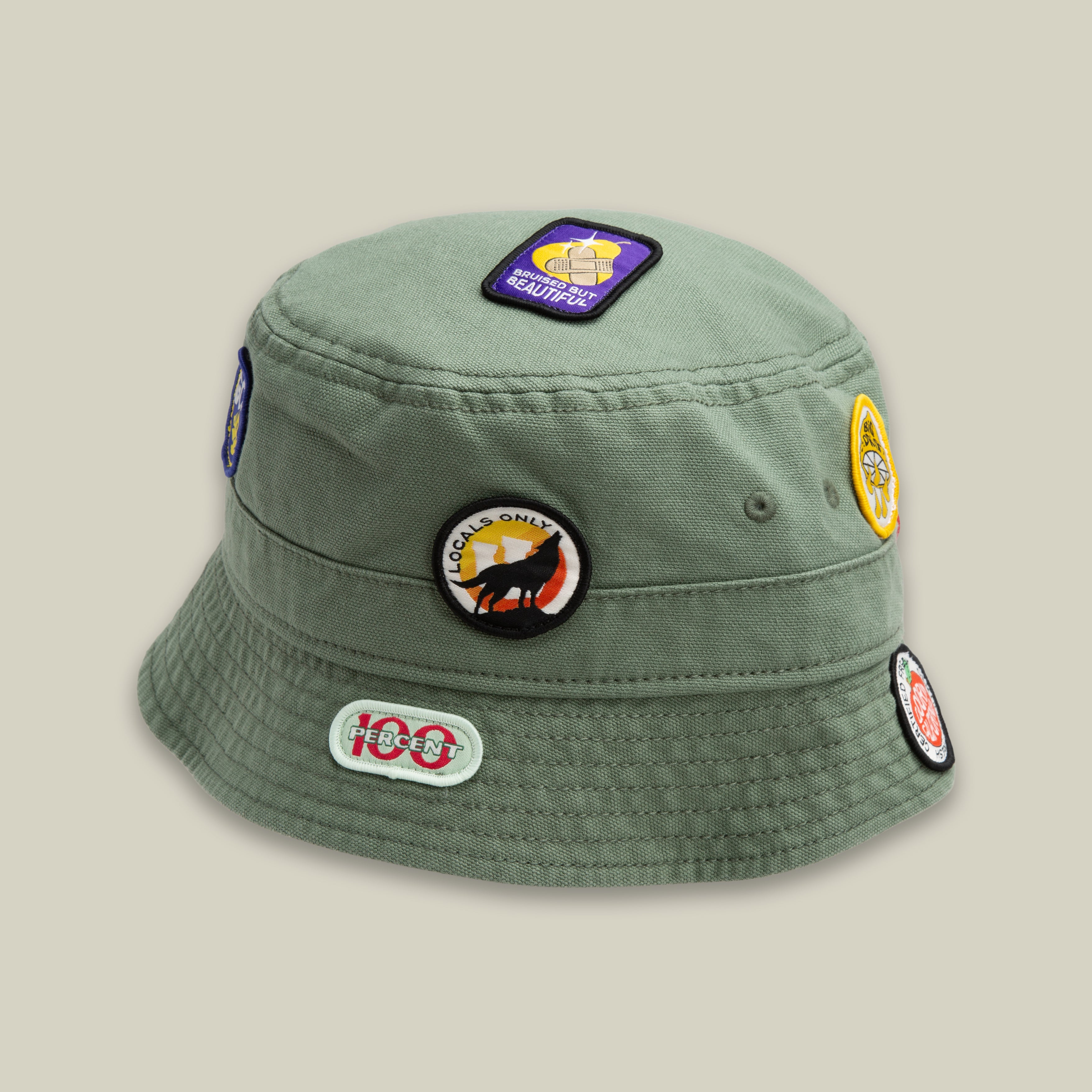 The Goorin Bros. PLU 1895 SHADE bucket hat features colorful embroidered patches on the top and sides, making it stand out like a walking bulletin board when displayed against a plain light background.