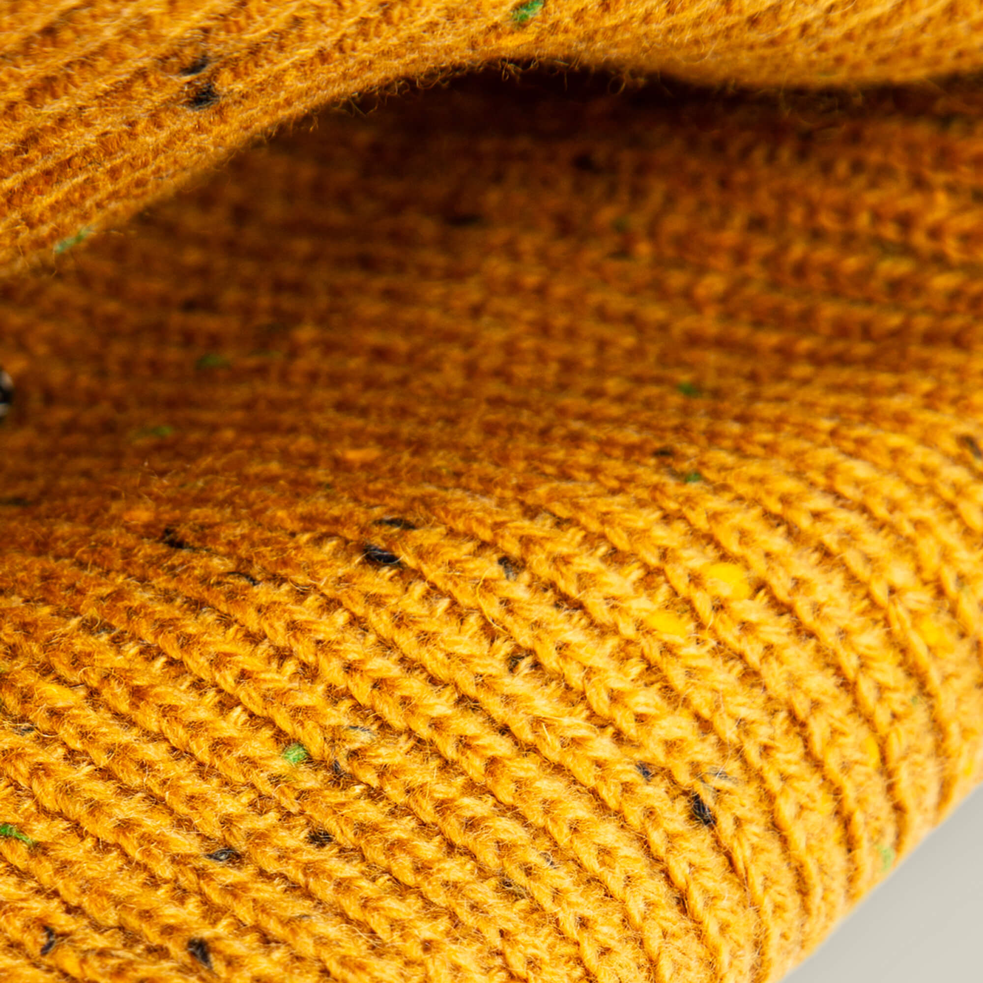 Close-up of folded, textured yellow knitted fabric with dark flecks from the No Comply by Goorin Bros.—ideal for crafting a warm, speckled beanie.