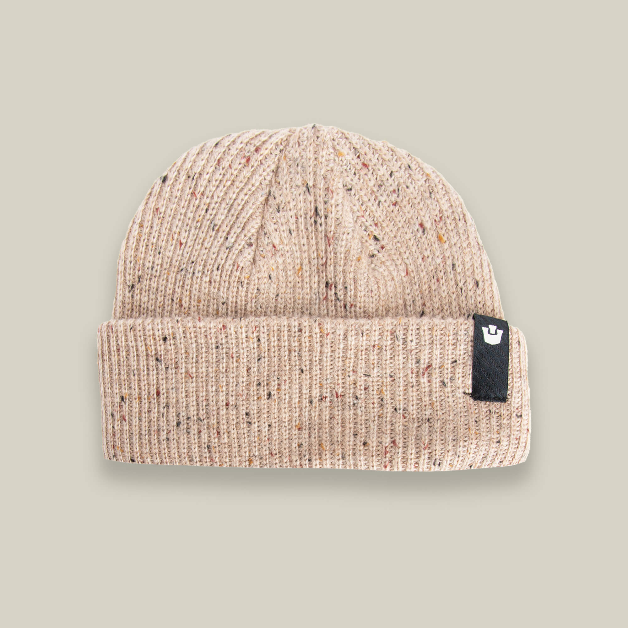 The Goorin Bros. No Comply beanie is a beige ribbed knit with multicolored speckles and a black rectangular logo tag on the folded brim, shown against a light gray background.