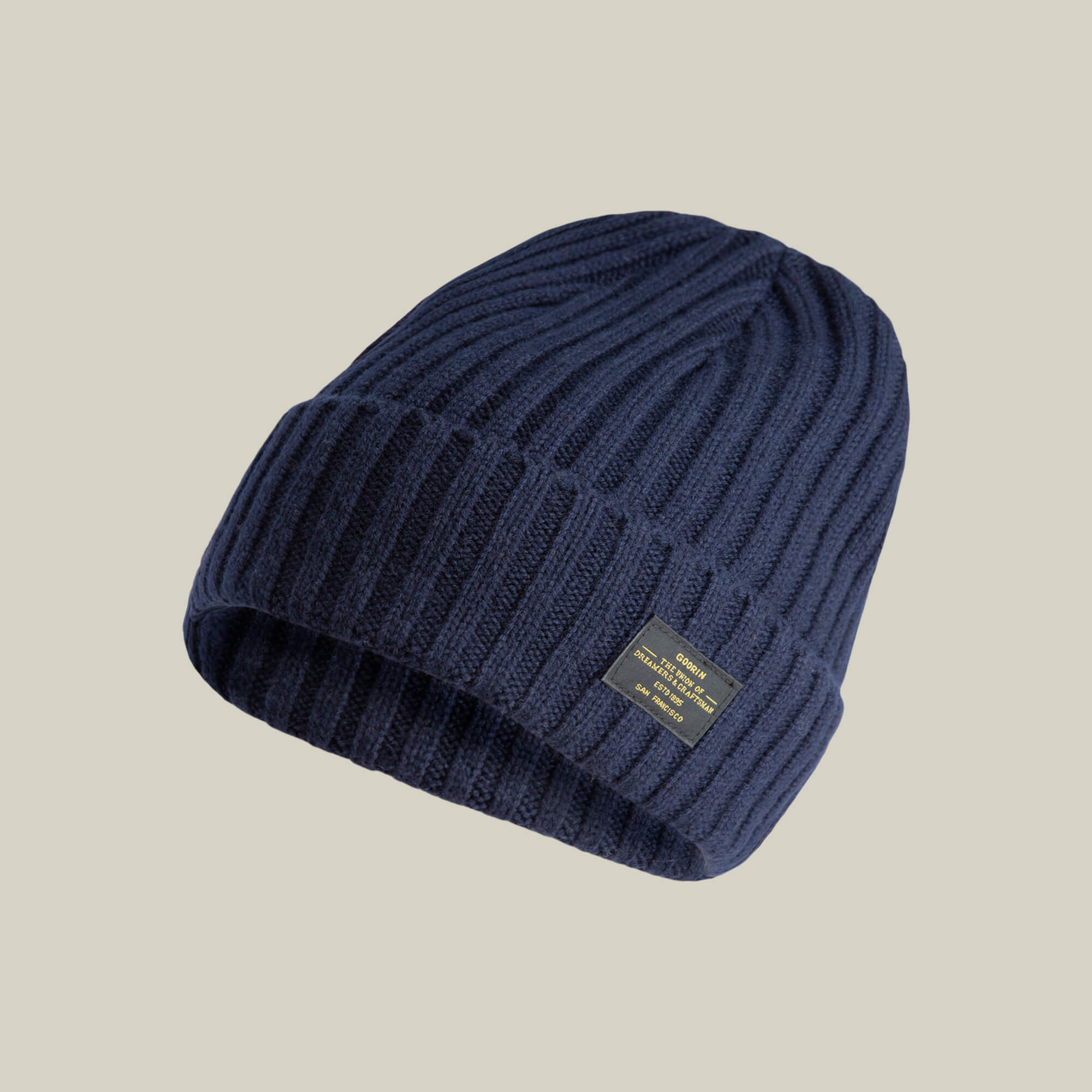 The Dream Cap by Goorin Bros. is a navy ribbed knit beanie made from cashmere wool, featuring a folded brim and a small rectangular black and gold front label.