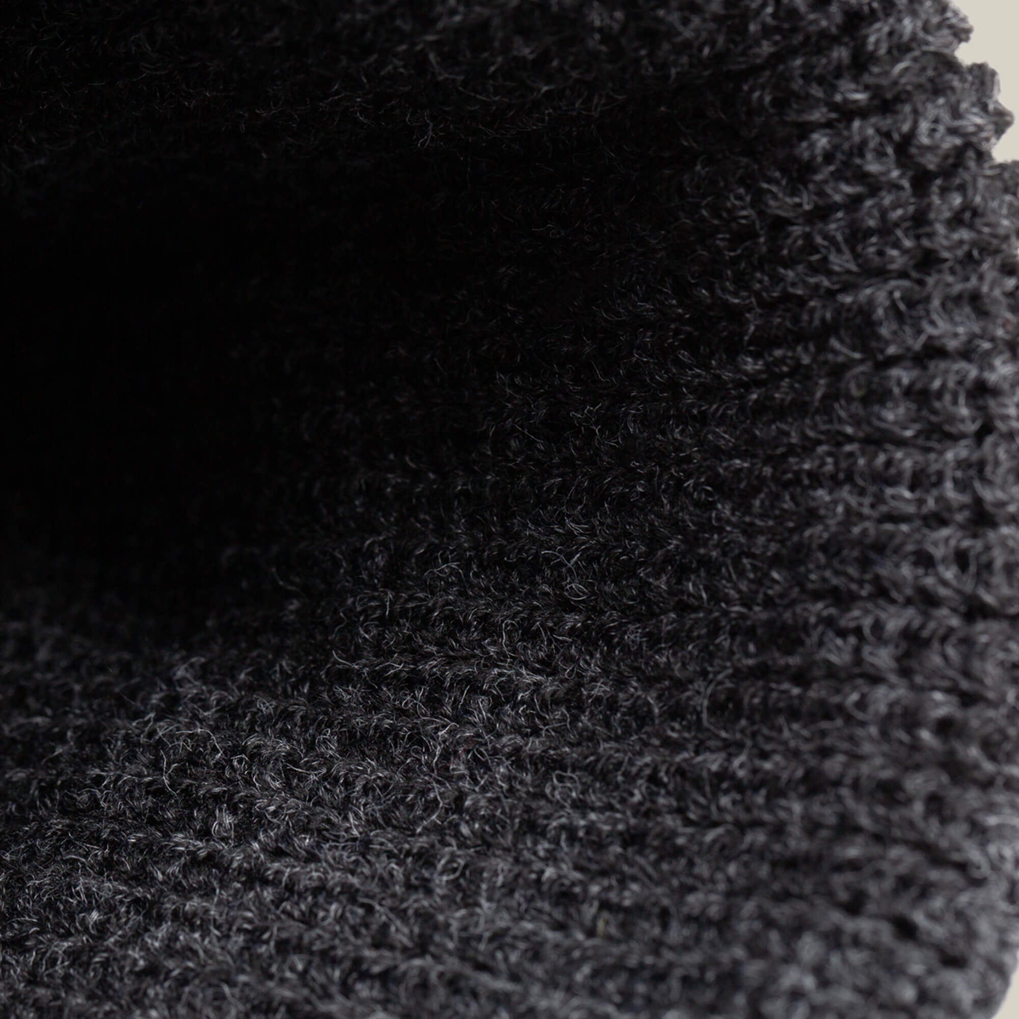 Close-up of textured, dark gray knitted fabric with visible loops and ribbed pattern, featured in The Guard Beanie by Goorin Bros.—a perfect cozy winter essential.