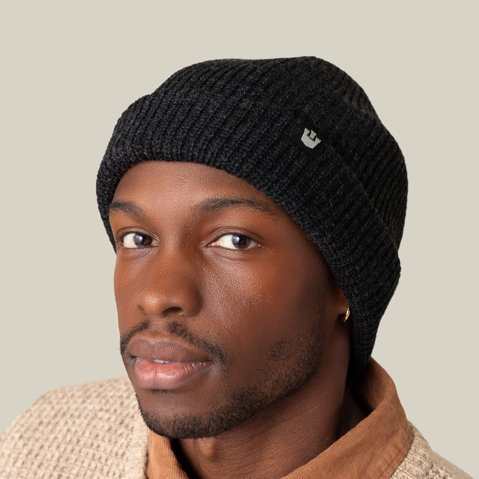 Wearing the Goorin Bros. Air to Fakie black watchman beanie, a beige textured sweater, and a brown collared shirt, a person looks directly at the camera against a neutral backdrop—perfect all-season attire.