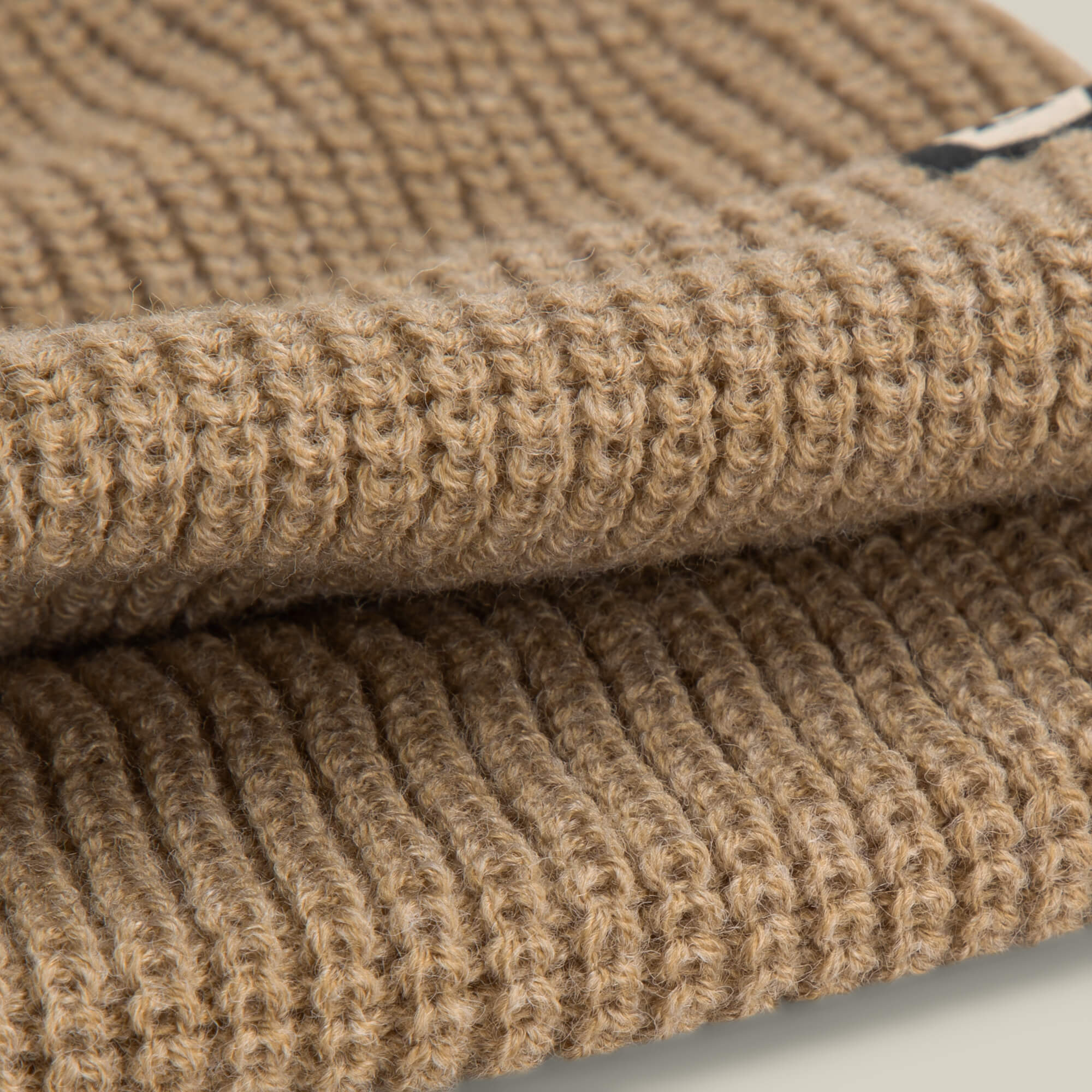 Close-up of two folded pieces of ribbed, tan knit fabric stacked on a light surface—crafted from lightweight poly knit, Air to Fakie by Goorin Bros. is a perfect all-season choice for styles like the classic watchman beanie.